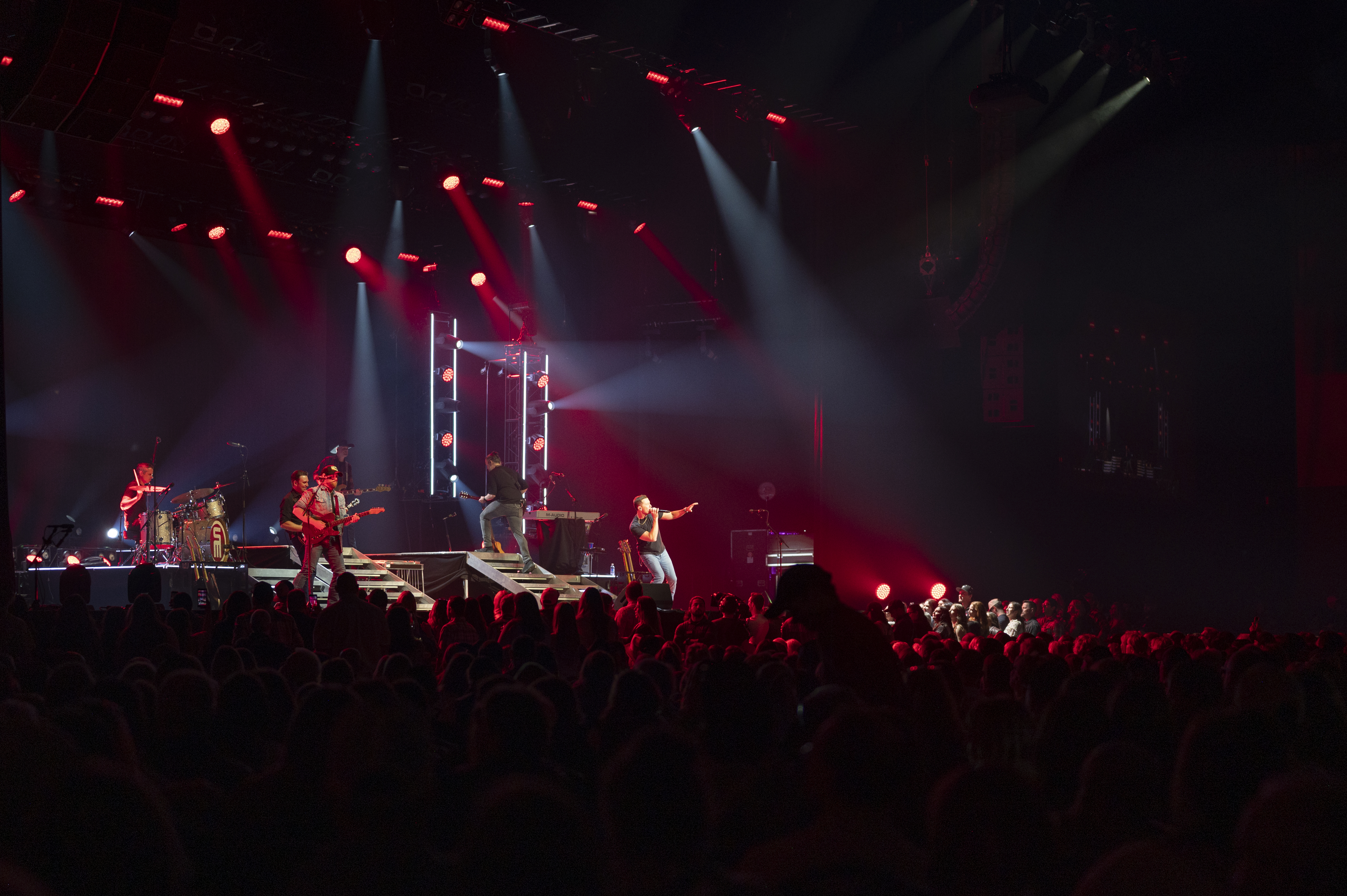 Scotty McCreery performs on stage with band members, illuminated by red and white lights