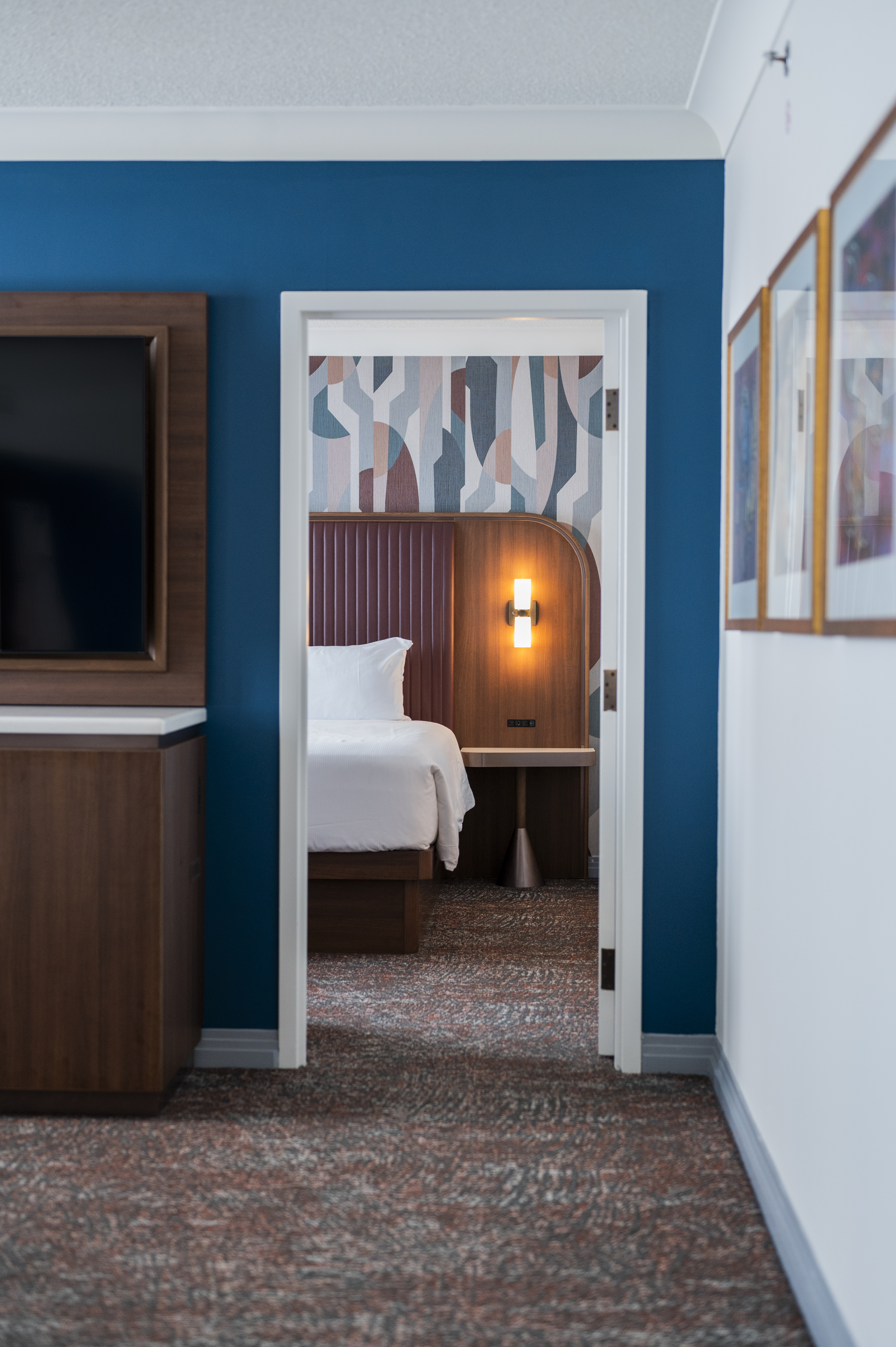 Doorway from hotel room into a bedroom suite with a king-size bed and modern furnishings