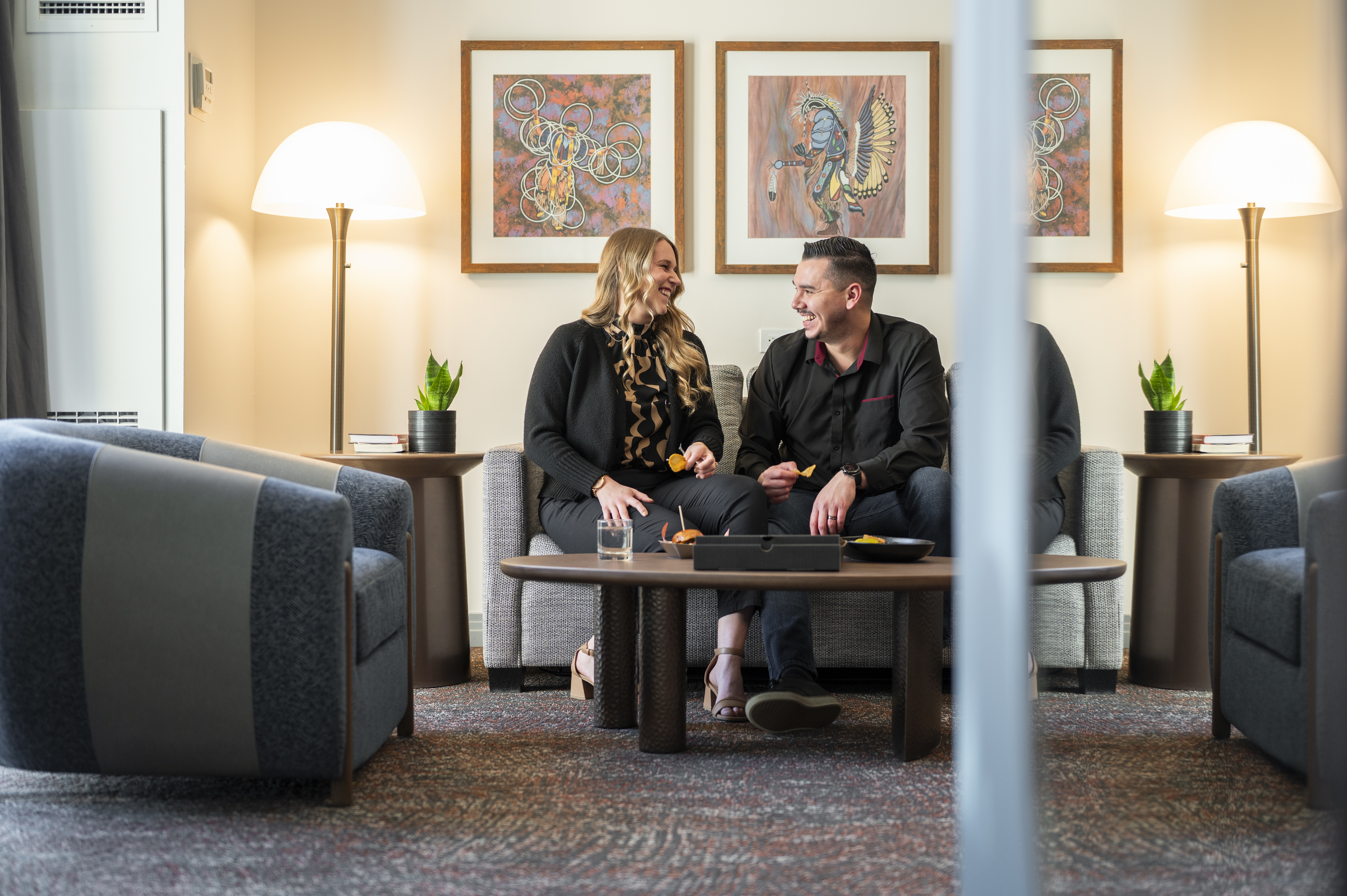 Man and woman laughing and eating snacks in a modern hotel suite