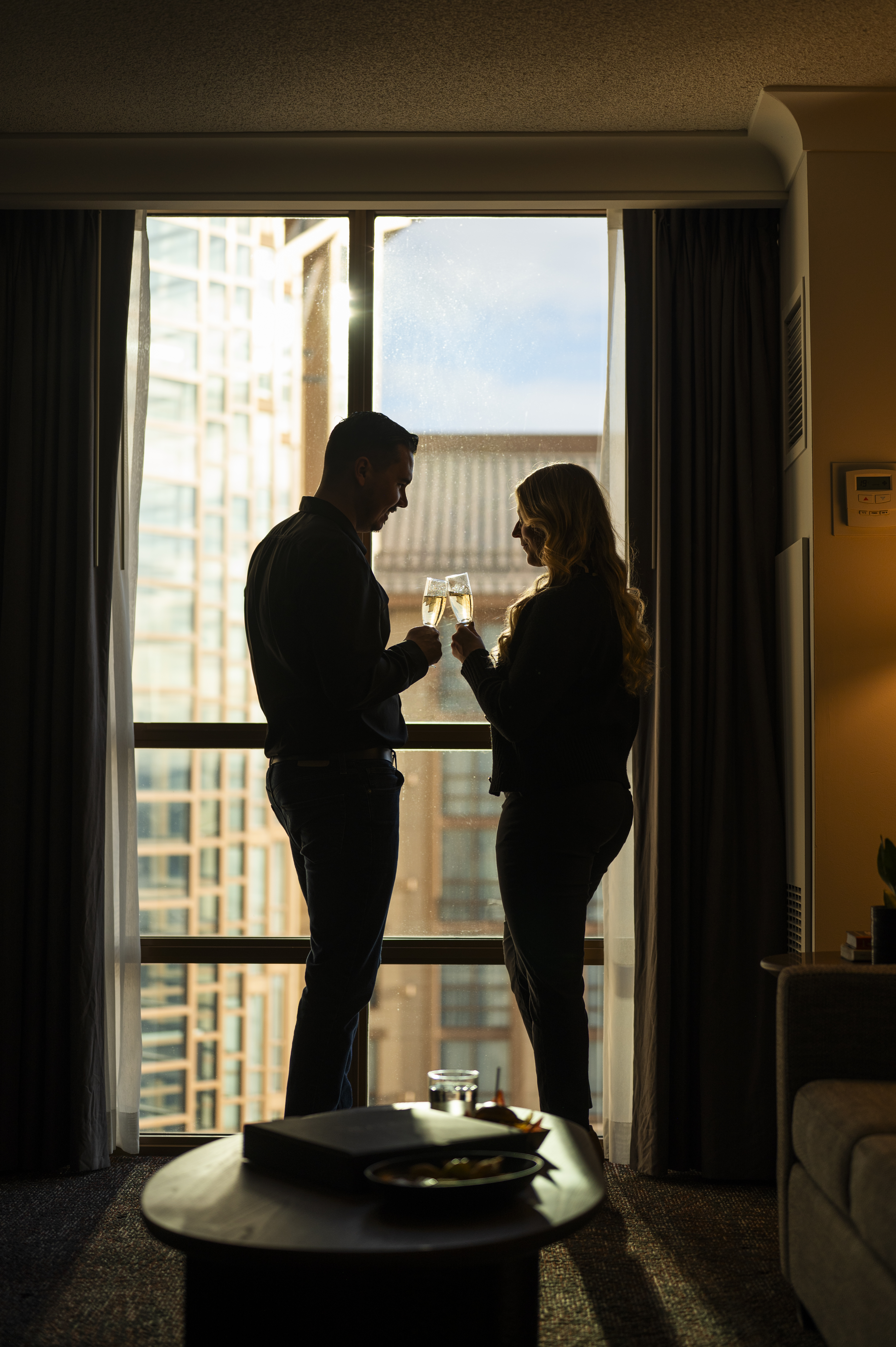 Silhouetted couple raises champagne glasses as they toast in a hotel suite