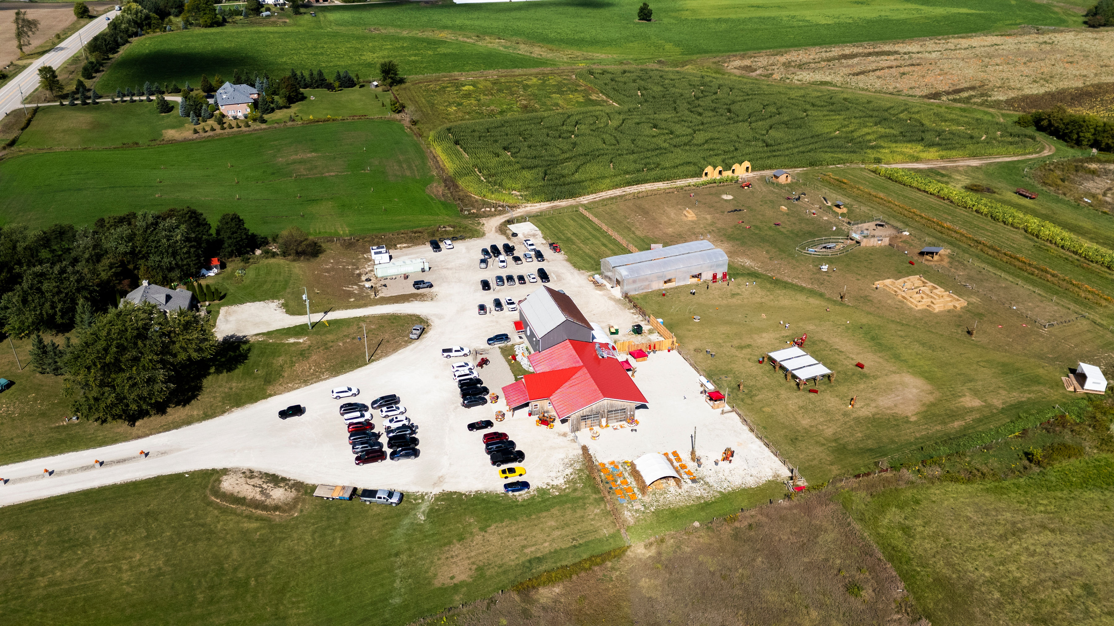 Aerial view of a Dufferin County farm with red-roofed buildings, corn maze, and parked cars
