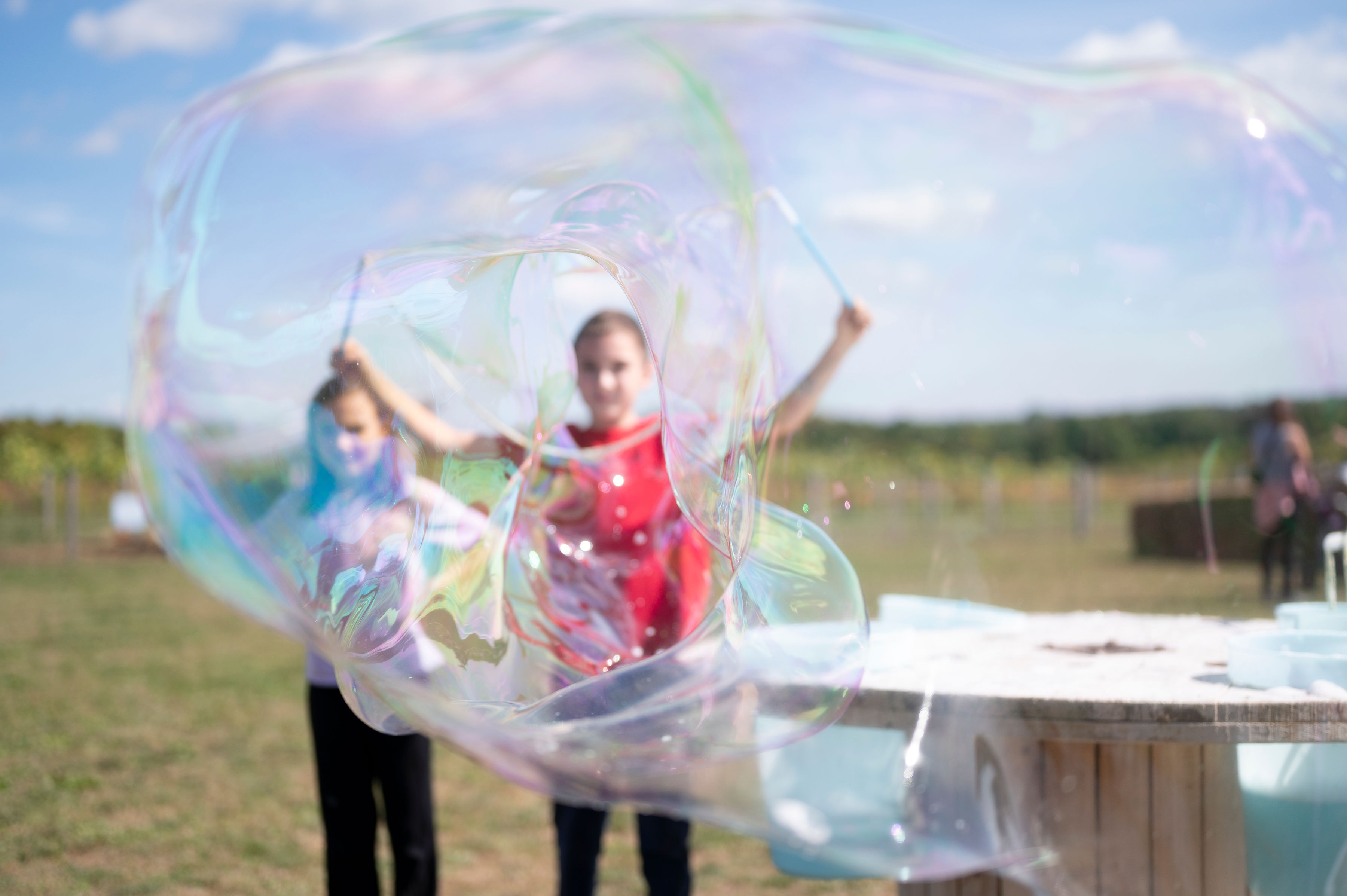 Two young girls create a giant iridescent bubble outdoors on a sunny day