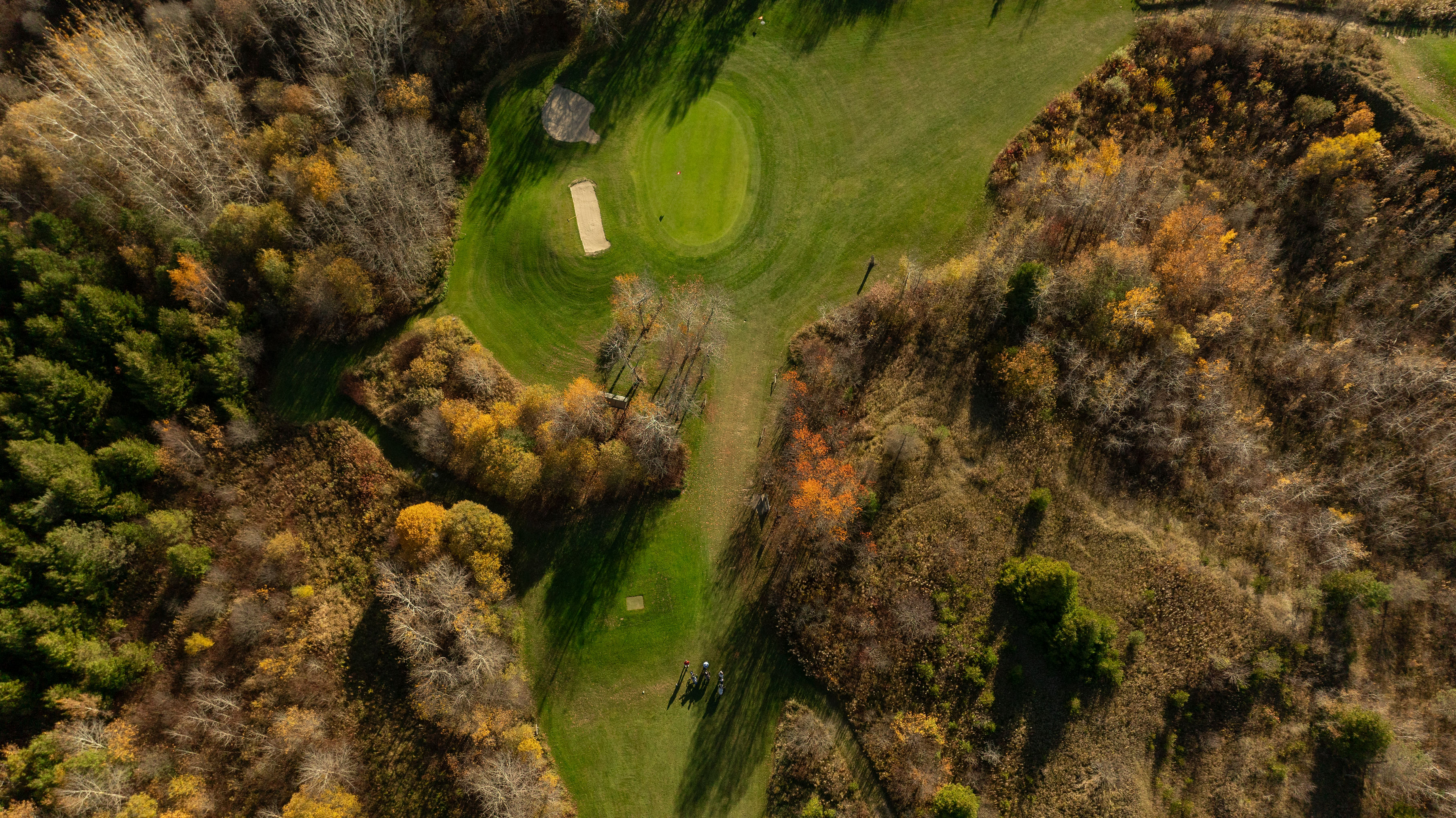 Aerial view of a vibrant green golf course surrounded by autumn trees and meadows