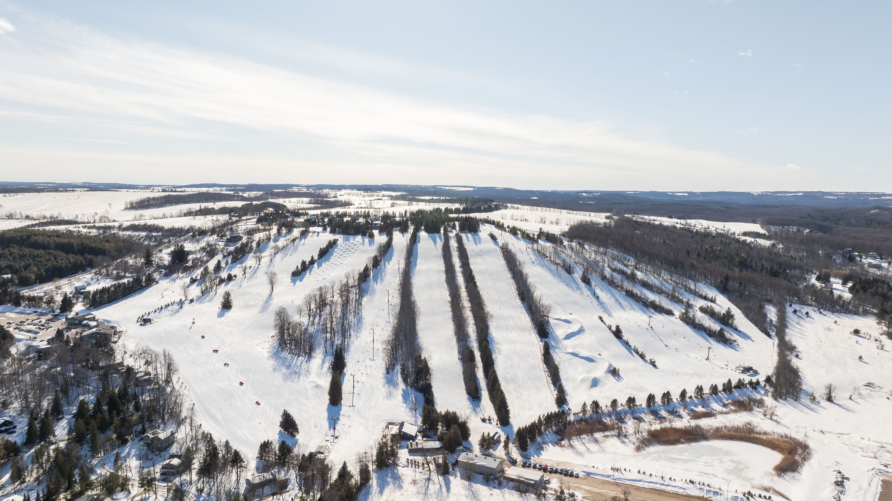 Aerial view of a snow-covered ski hill with pistes and surrounding pine forests