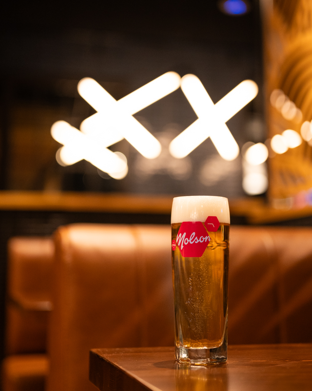 Glass of Molson beer on a wooden table in a restaurant setting with illuminated decor