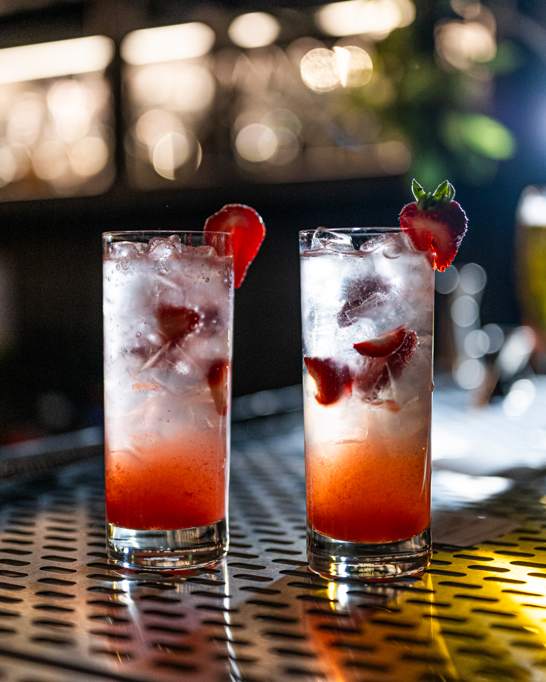 Two refreshing strawberry cocktails with ice and fruit on a shiny bar top