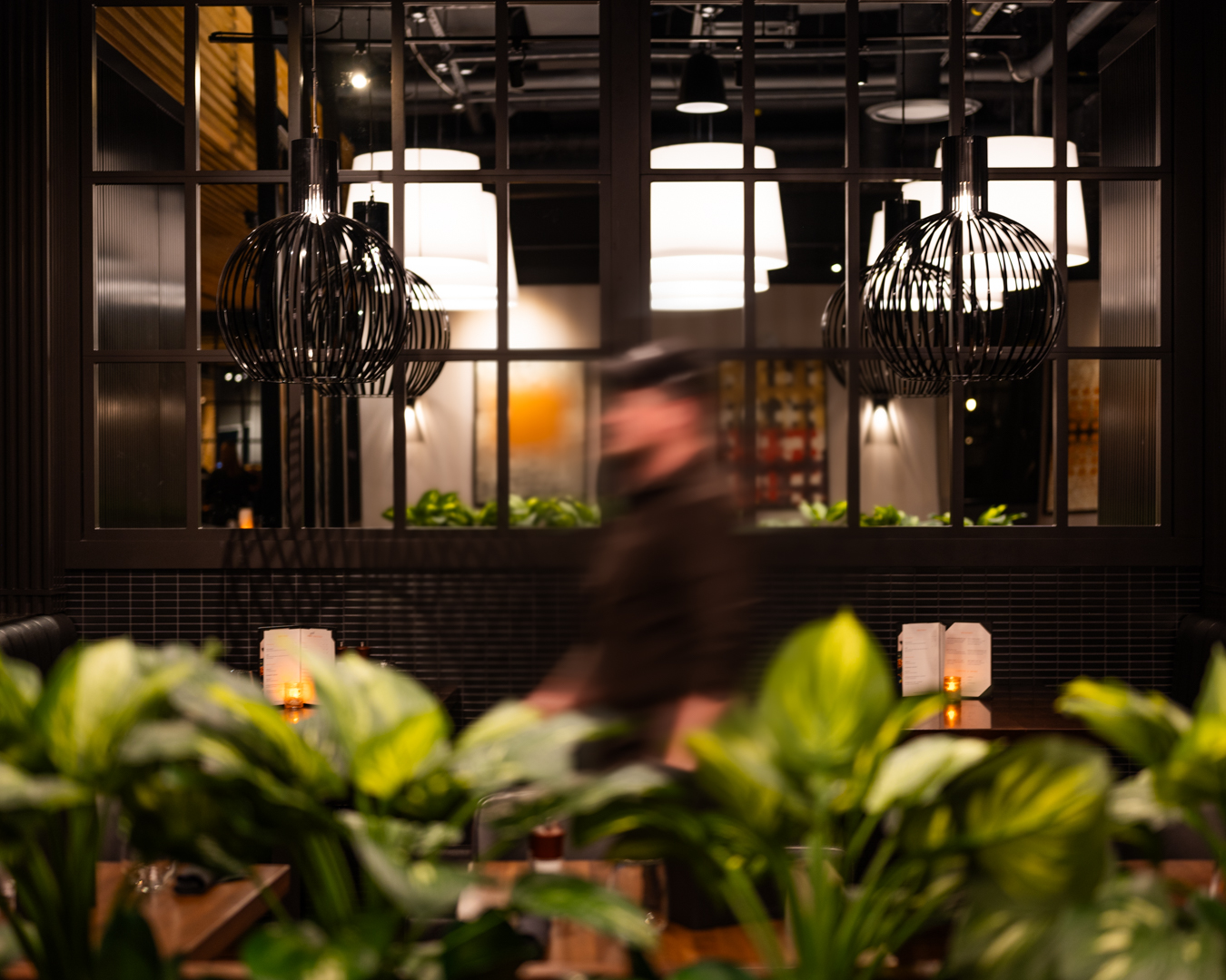 Milestones restaurant interior with modern lighting, blurred person, and plants in foreground
