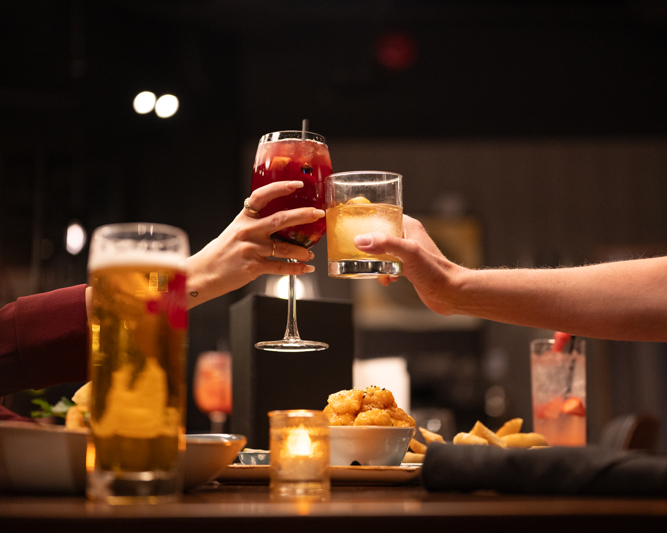 Two hands clinking a red cocktail and amber whiskey at a Milestones restaurant