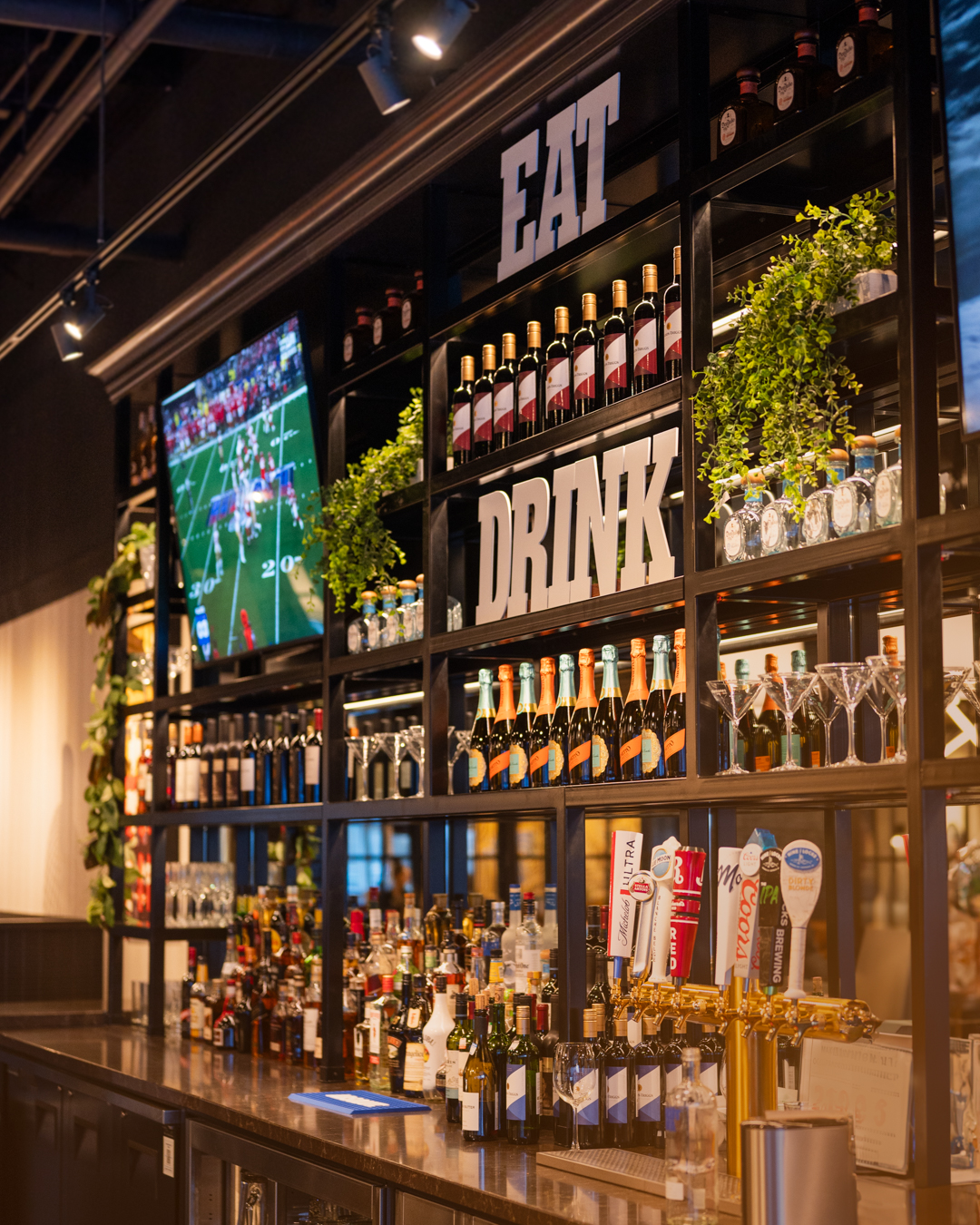 Well-stocked bar at Milestones restaurant with EAT and DRINK signs, TV showing football