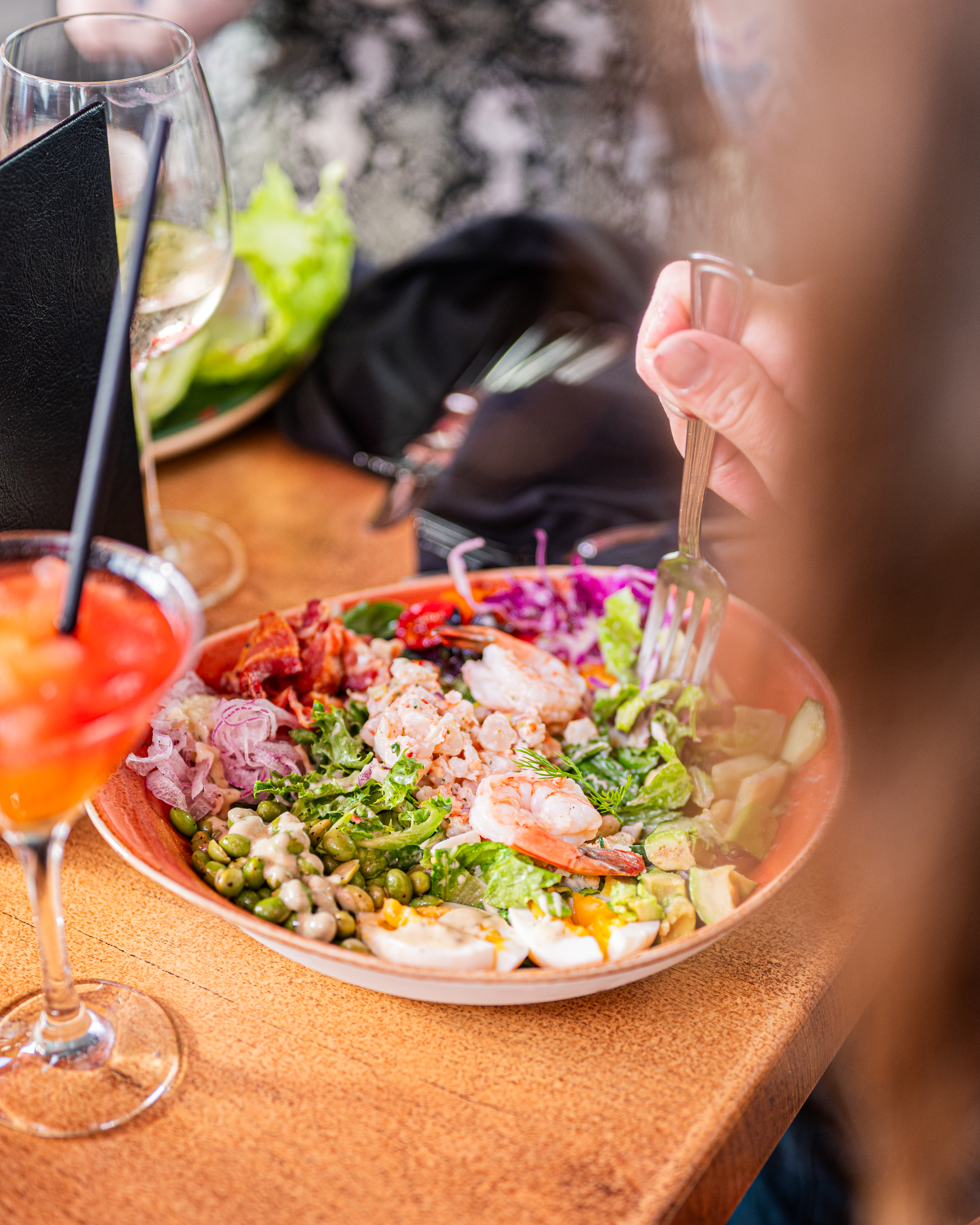 Person eating a fresh Milestones salad with shrimp, avocado, egg, and bacon