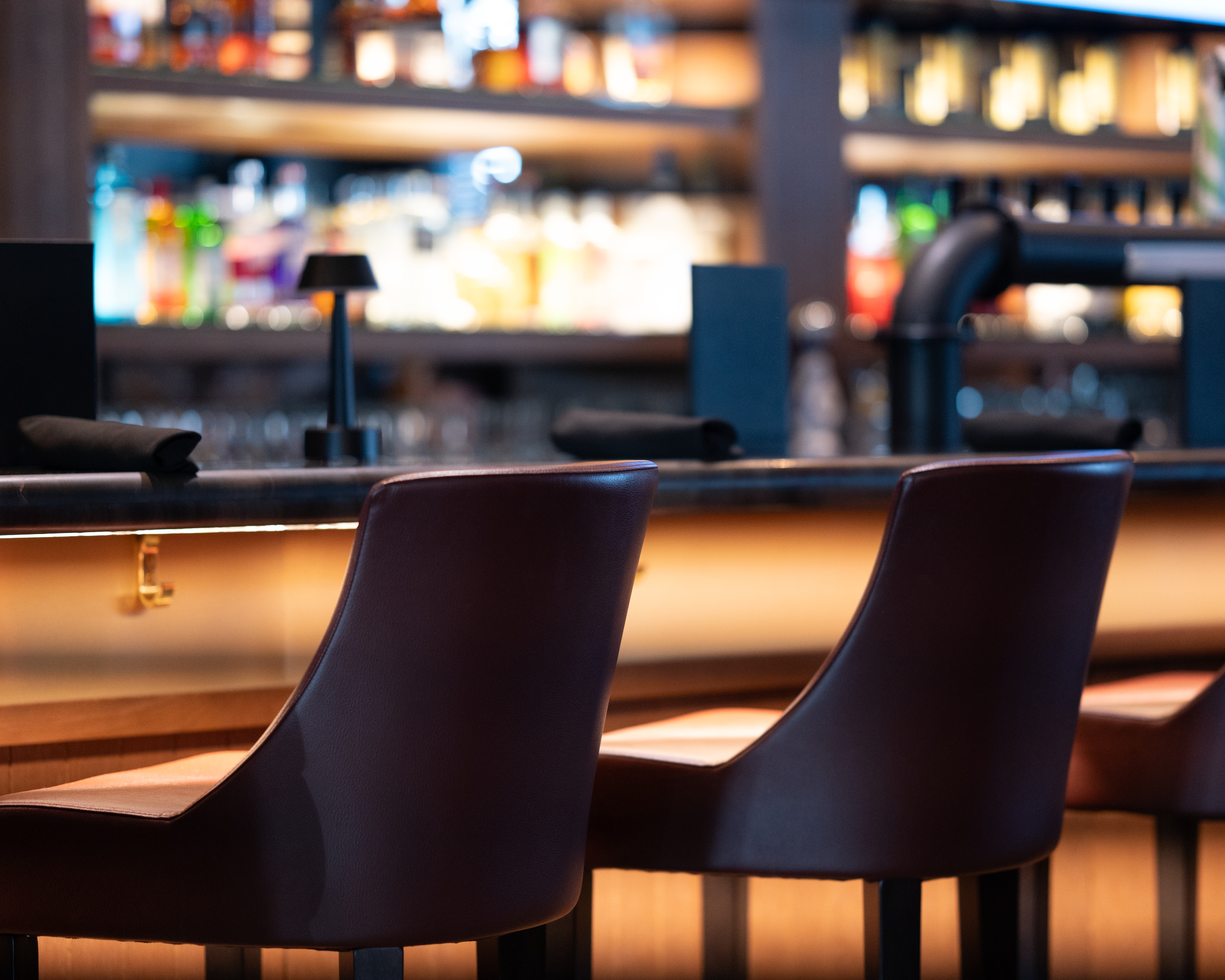 Empty bar stools at a Milestones restaurant bar with glowing bottles in the background