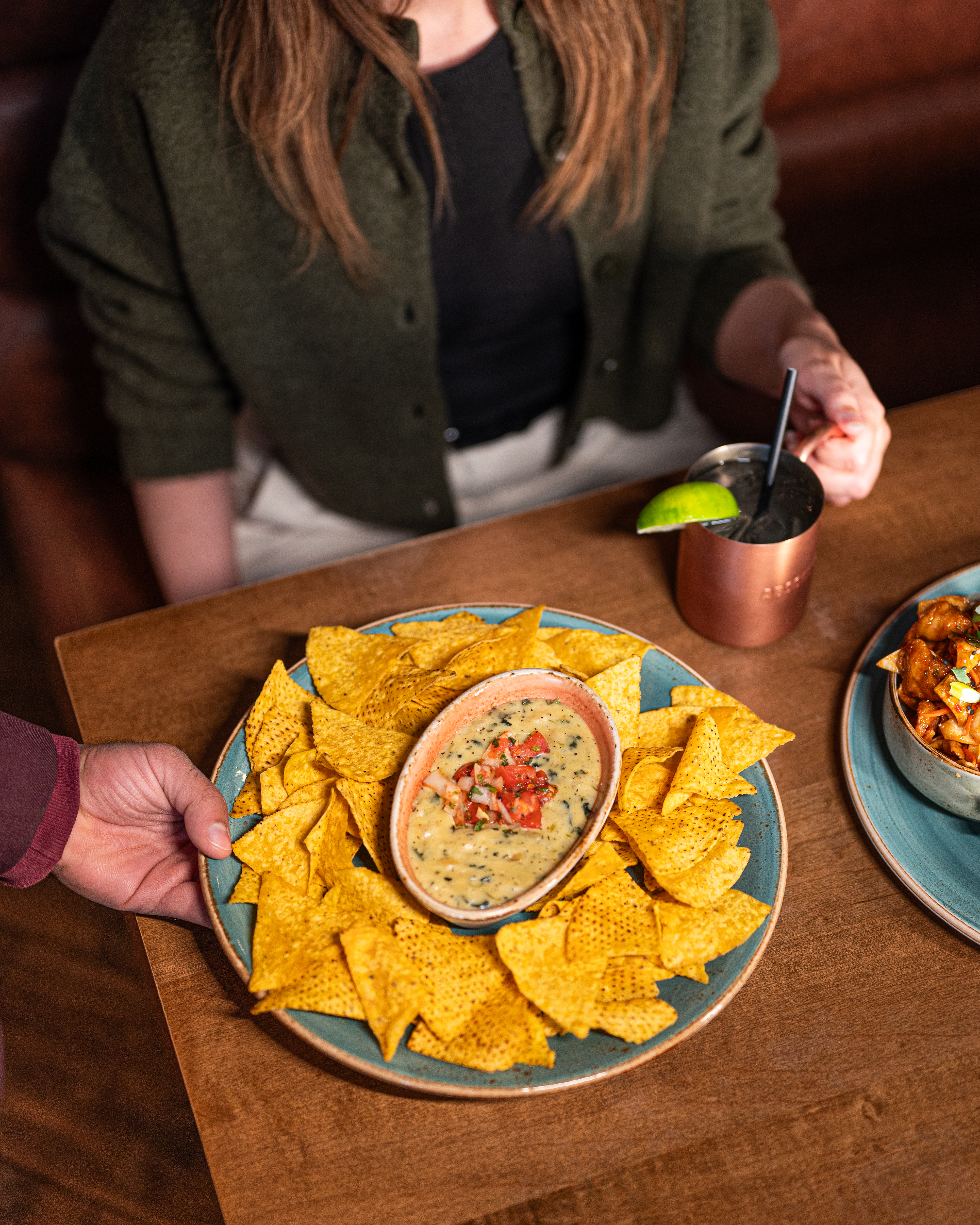 Server placing a plate of nachos with queso dip on a wooden table at Milestones
