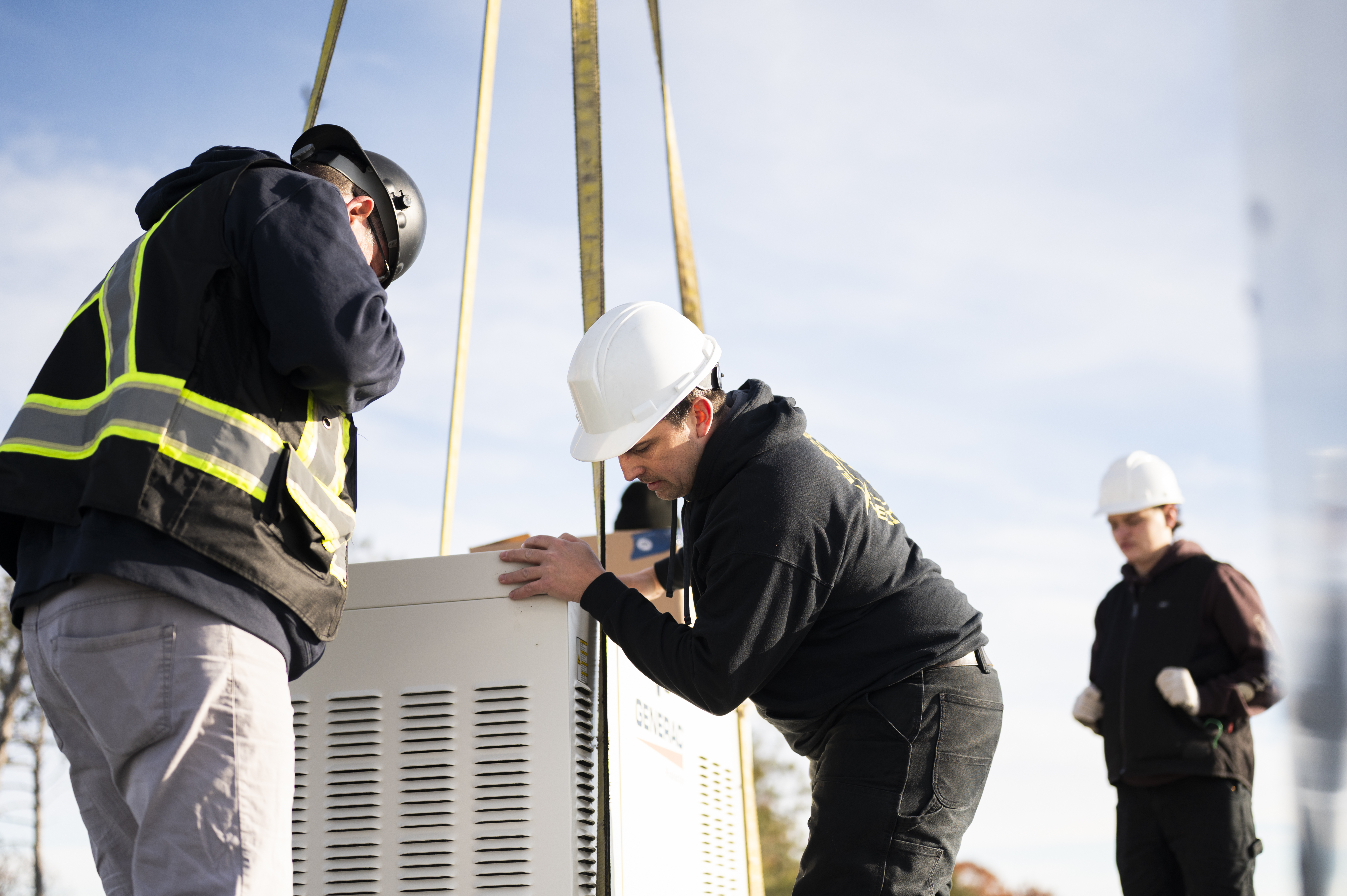 Electrical Elite team members installing large equipment with a crane on a sunny day
