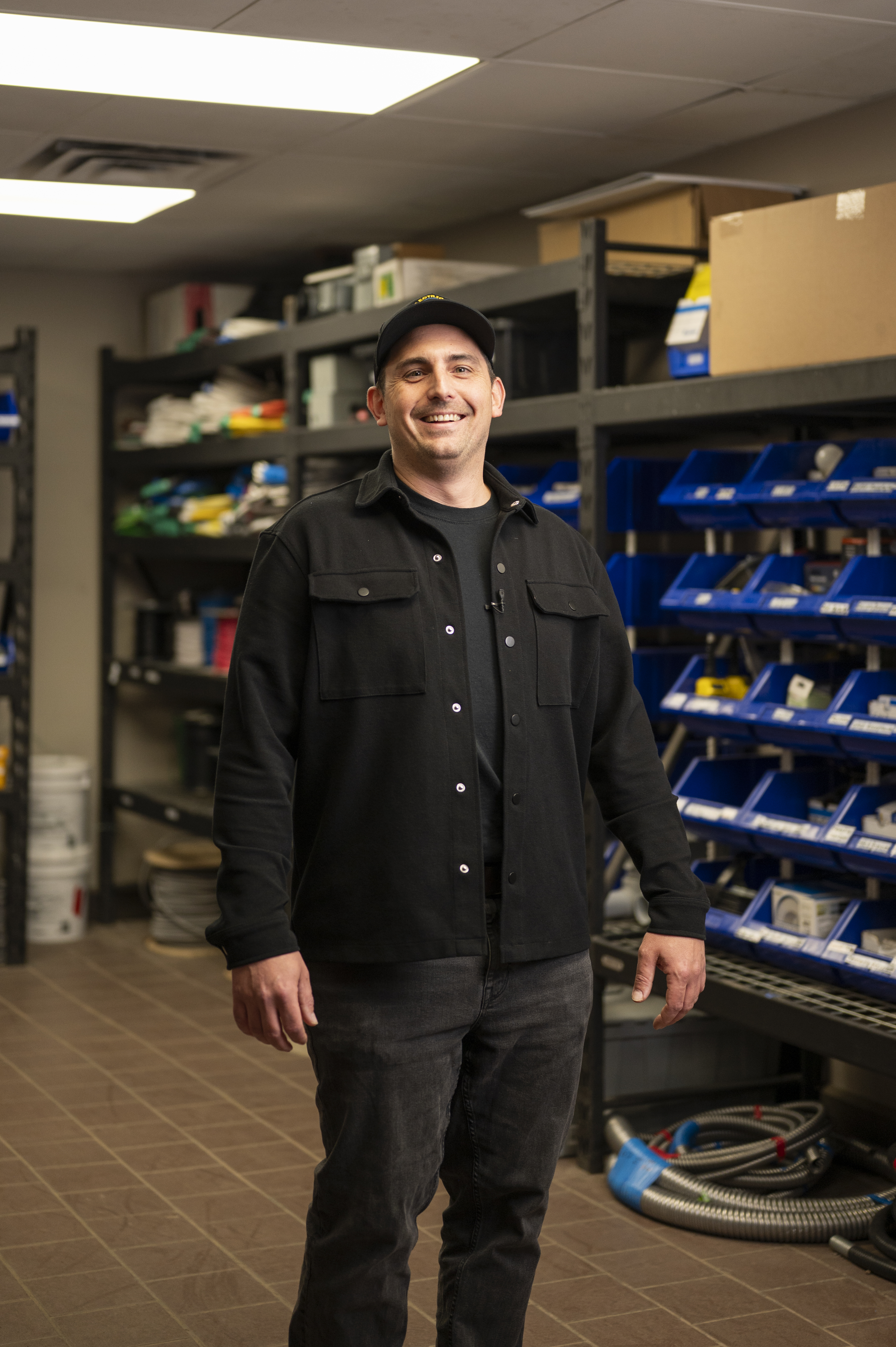Smiling man wearing a black cap and shirt standing in an electrical supply room
