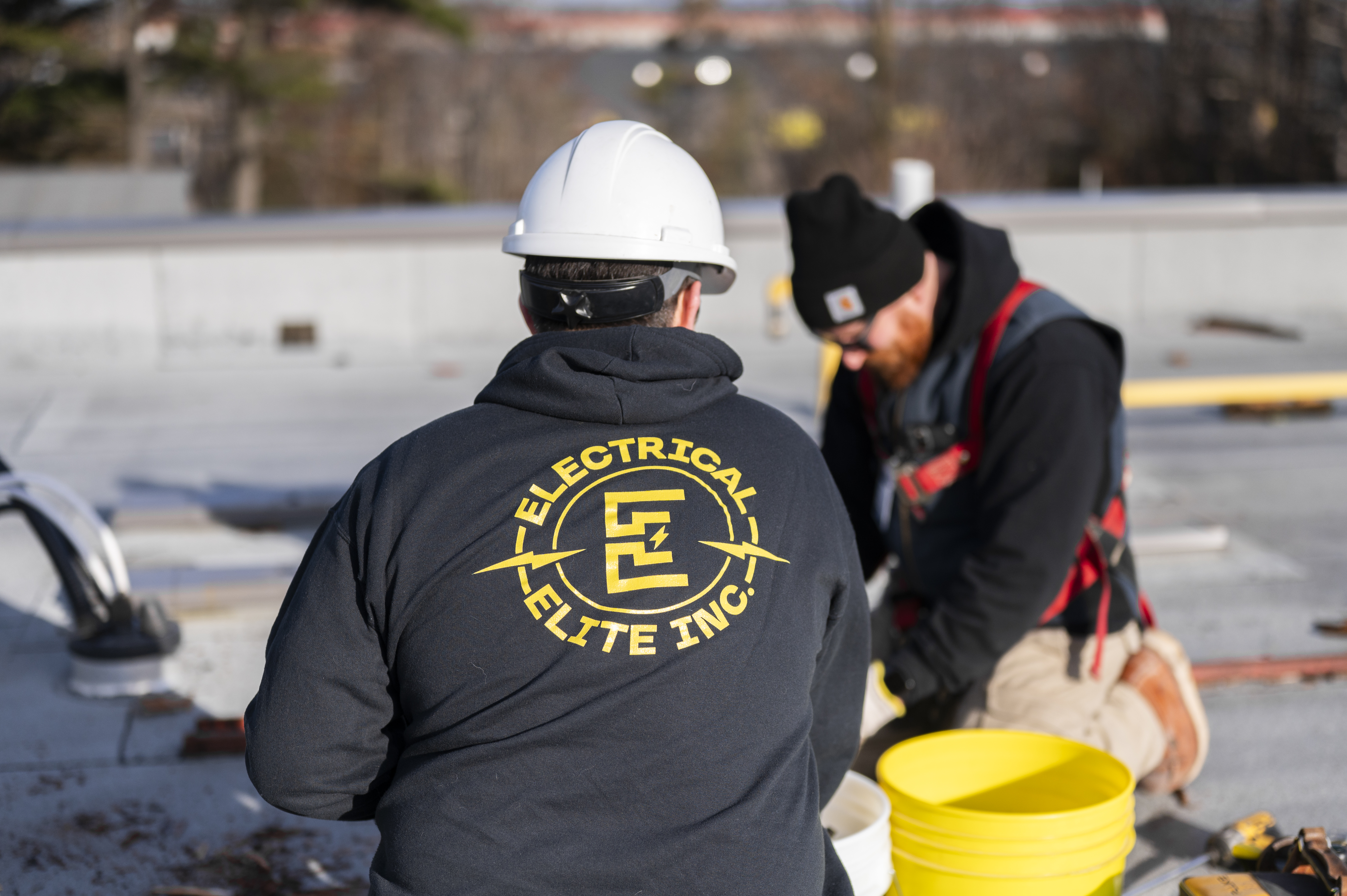 Two Electrical Elite construction workers on a rooftop, one wearing a logo hoodie