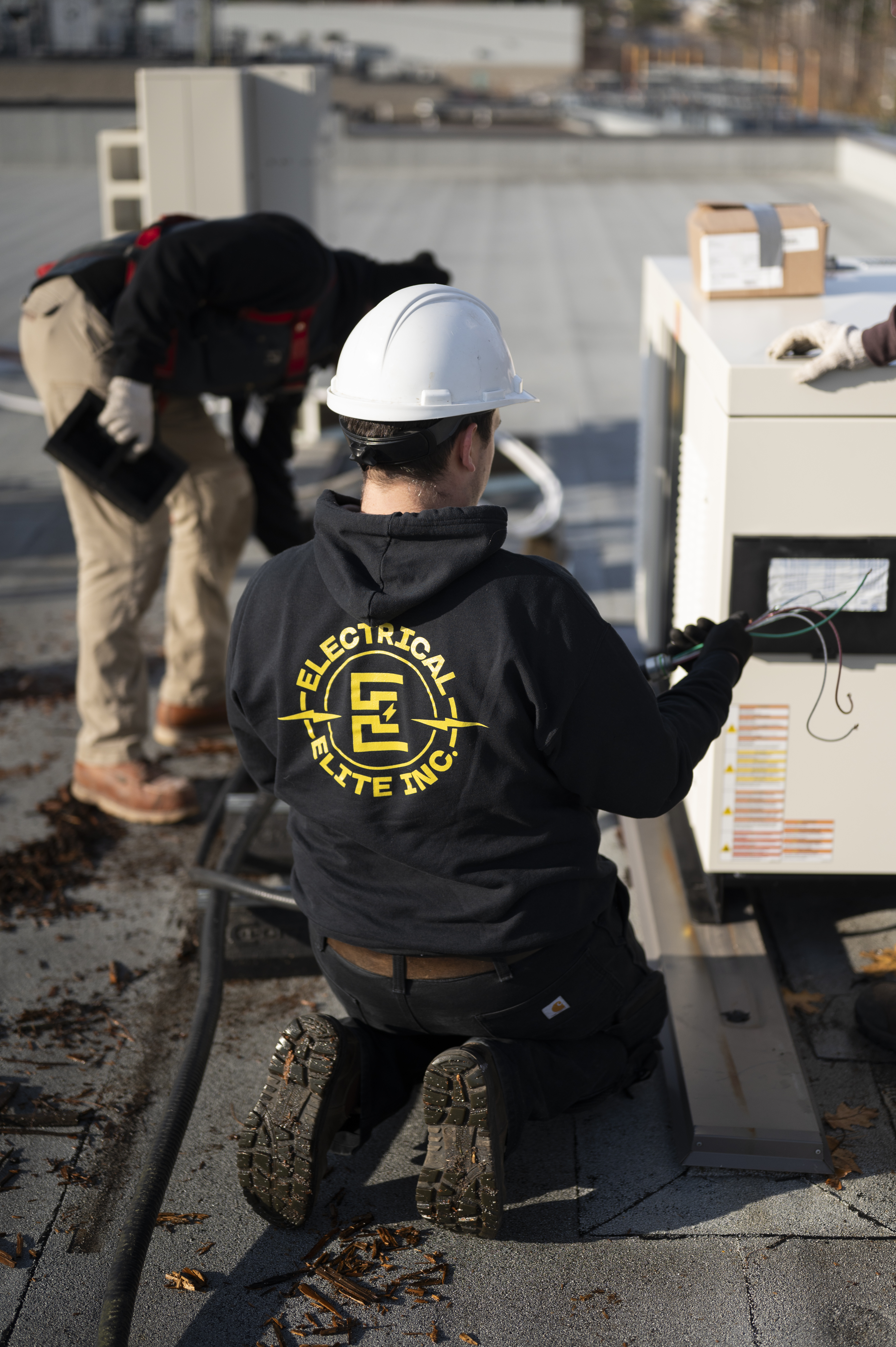 Electrical Elite technician wearing a hard hat, kneeling to connect wires on a rooftop