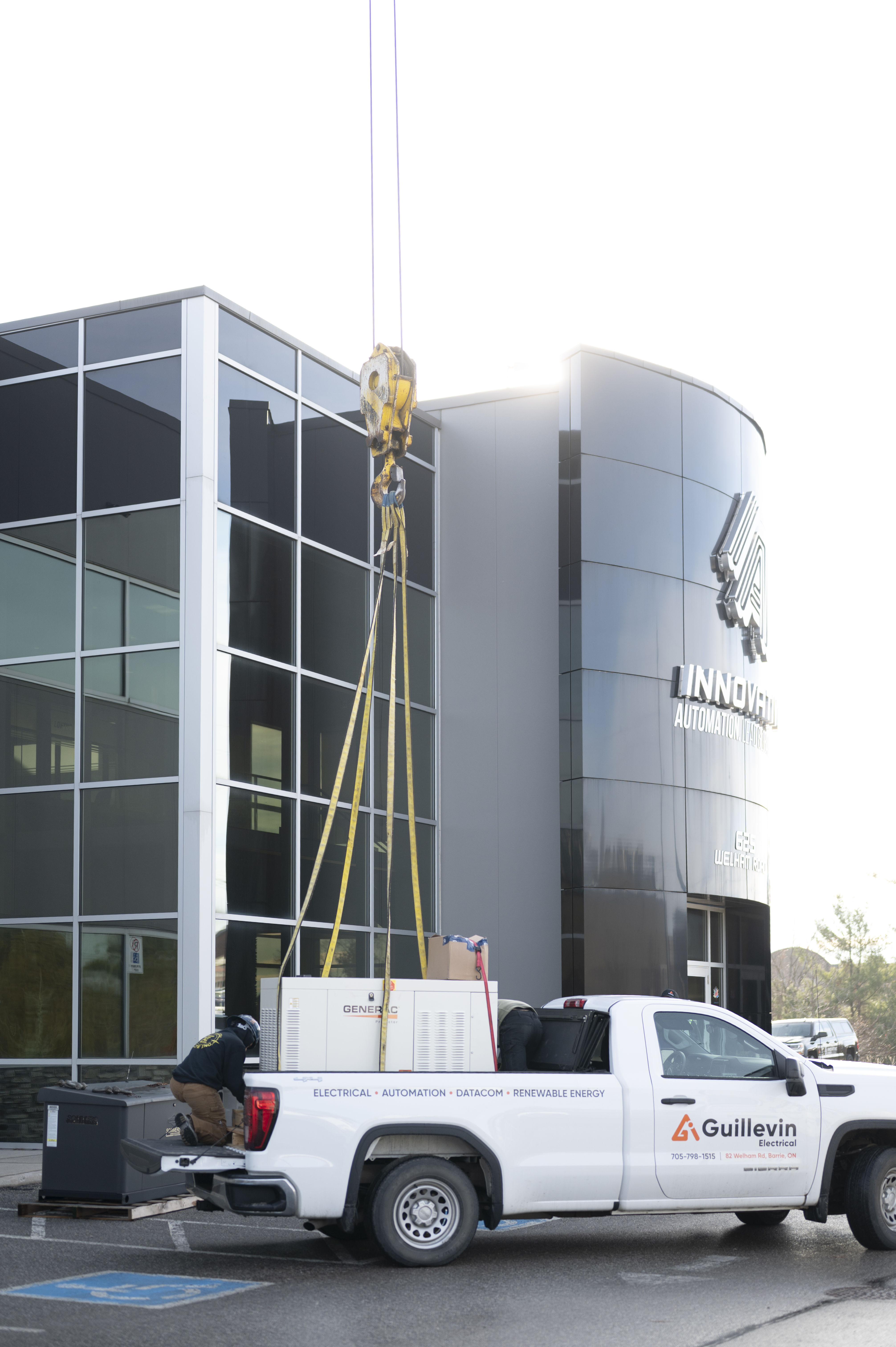 Worker near a truck and large generator being lifted by a crane at a commercial building