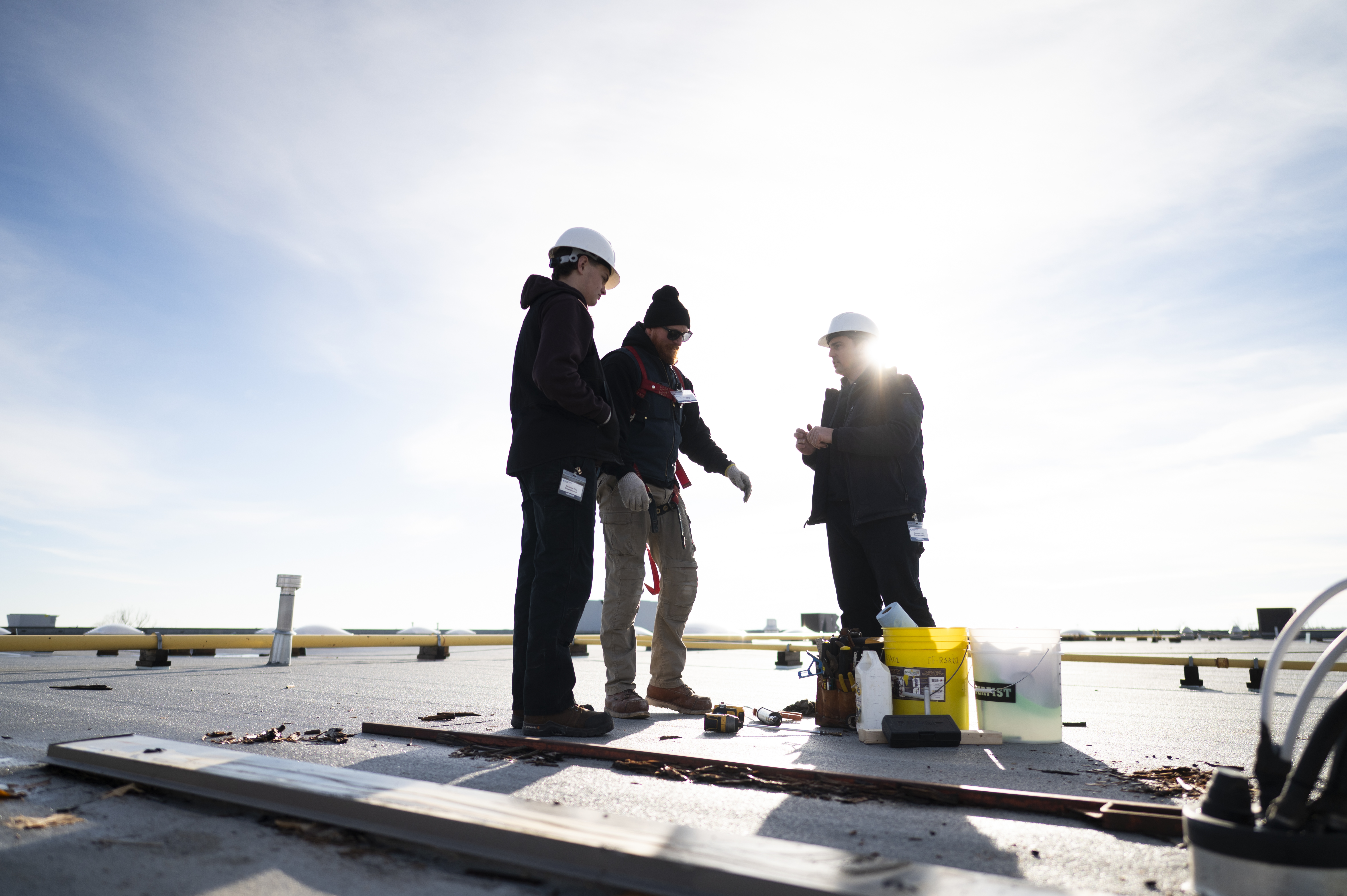 Three construction workers in hard hats discussing plans on a sunny rooftop