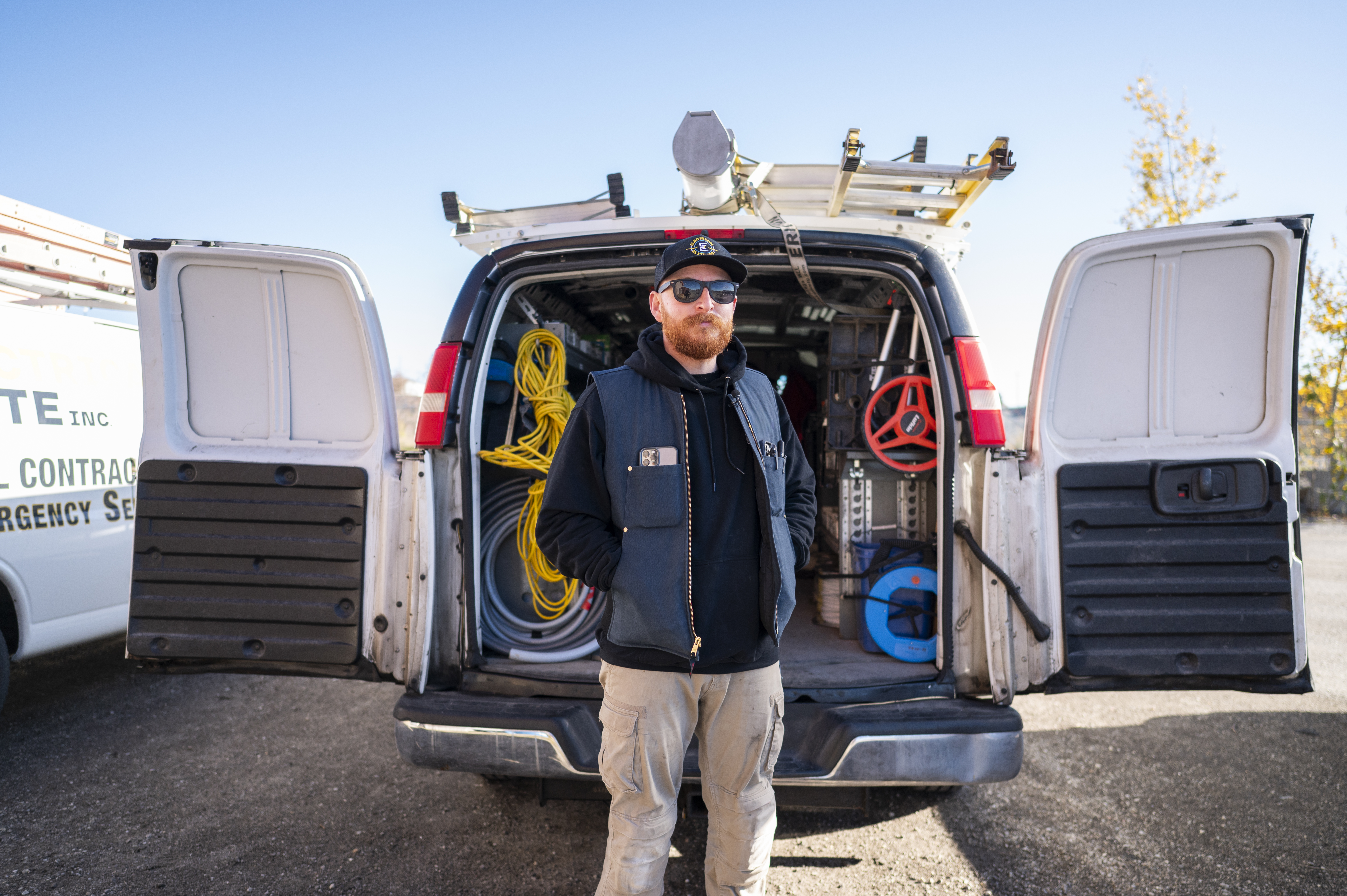 Construction worker with beard and sunglasses standing by an electrical work van