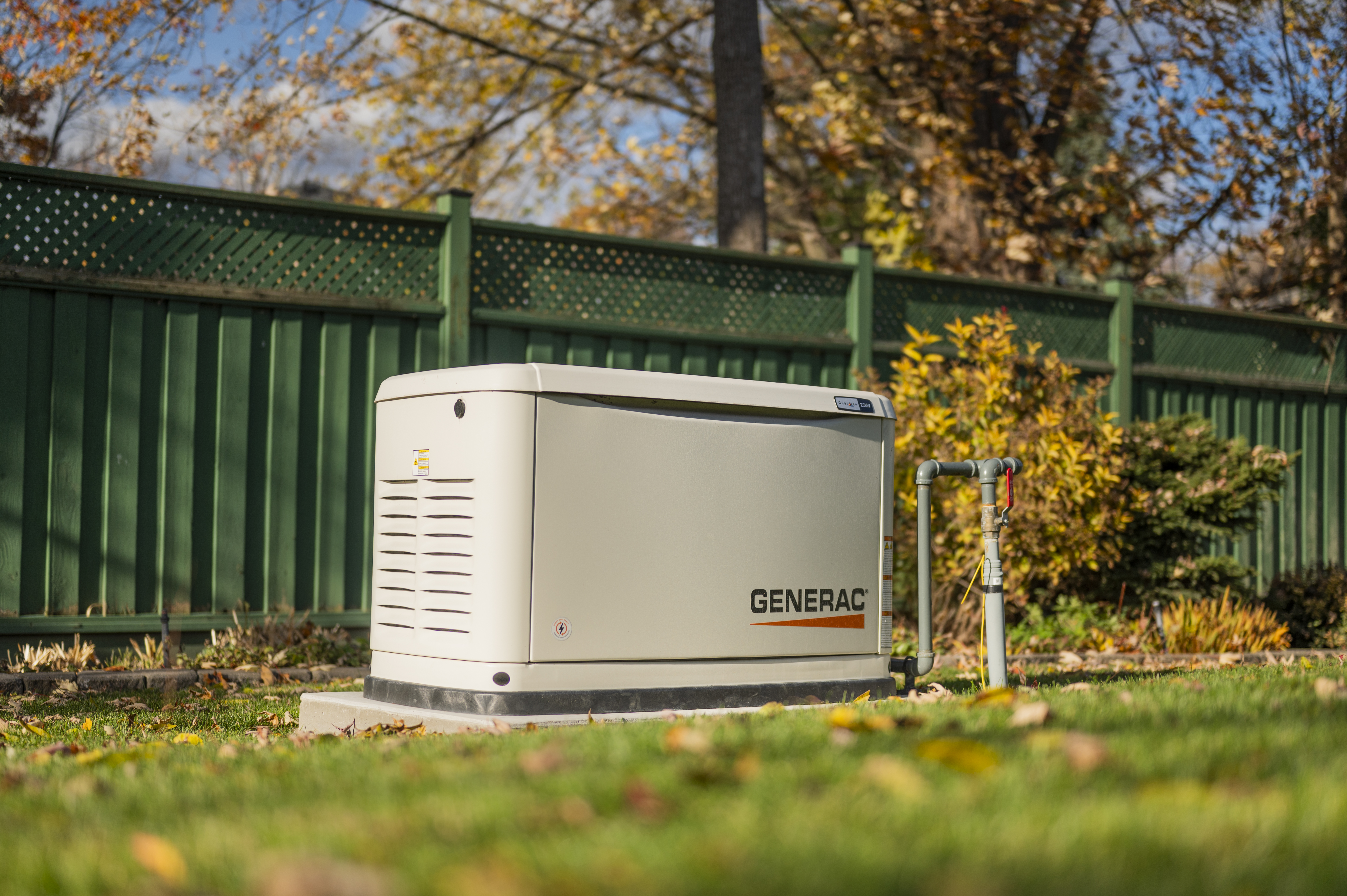 Generac home standby generator on concrete pad in green yard with fall foliage