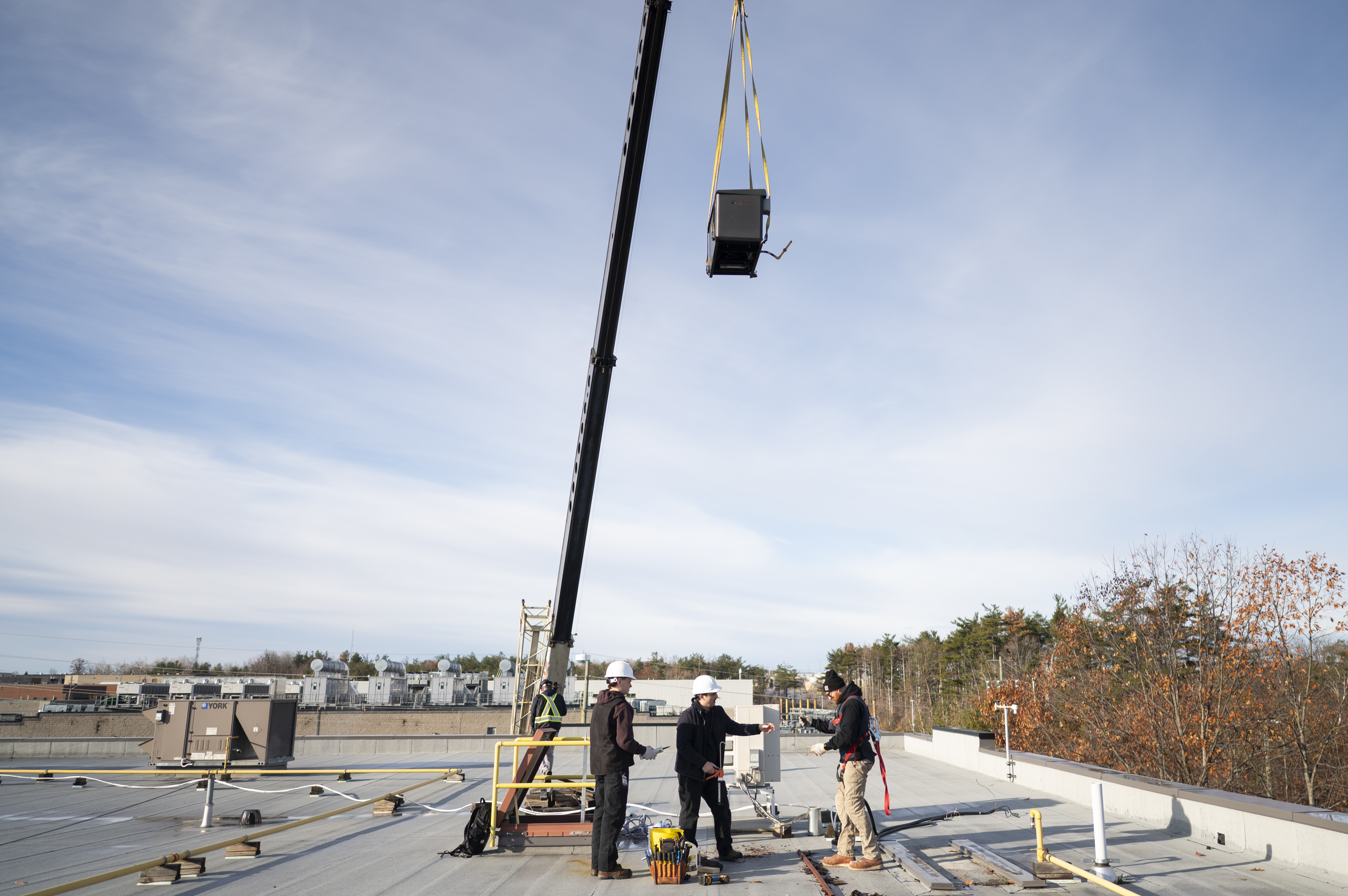 Construction crew on a rooftop, a crane lifting equipment against a clear sky