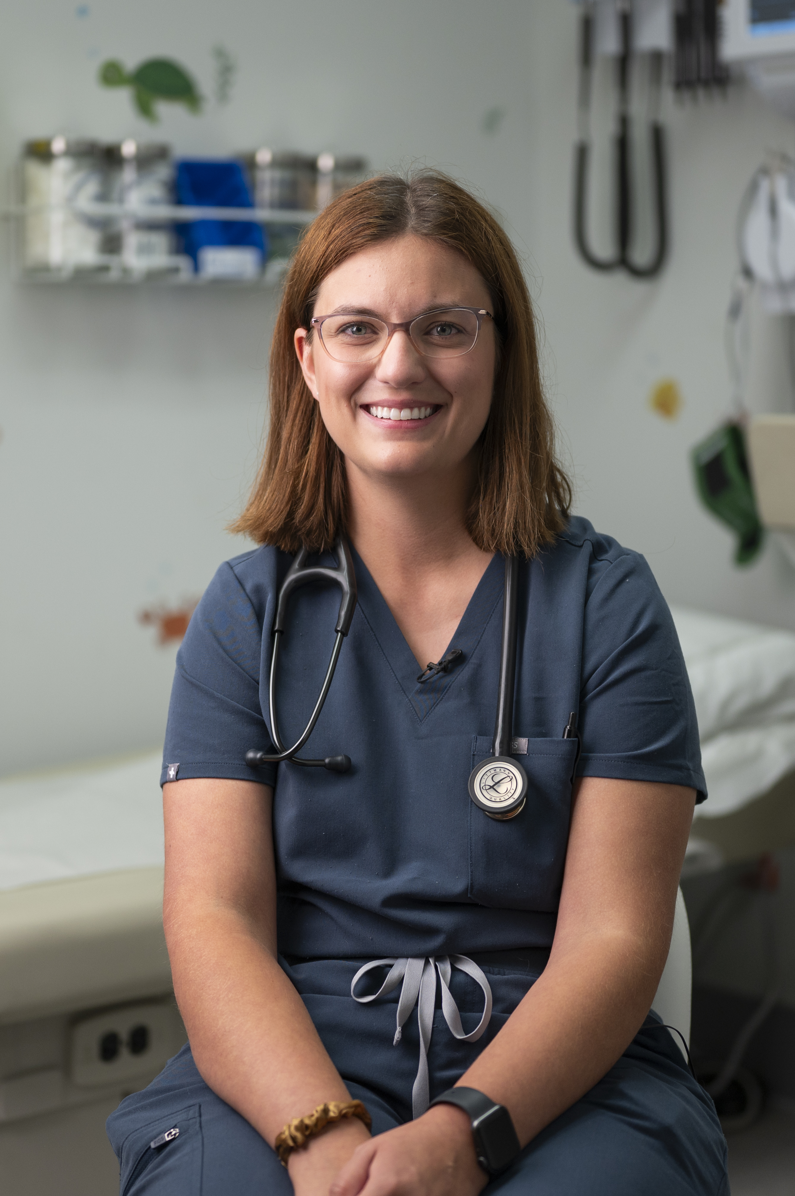 Smiling healthcare professional in blue scrubs with a stethoscope in a clinic examination room
