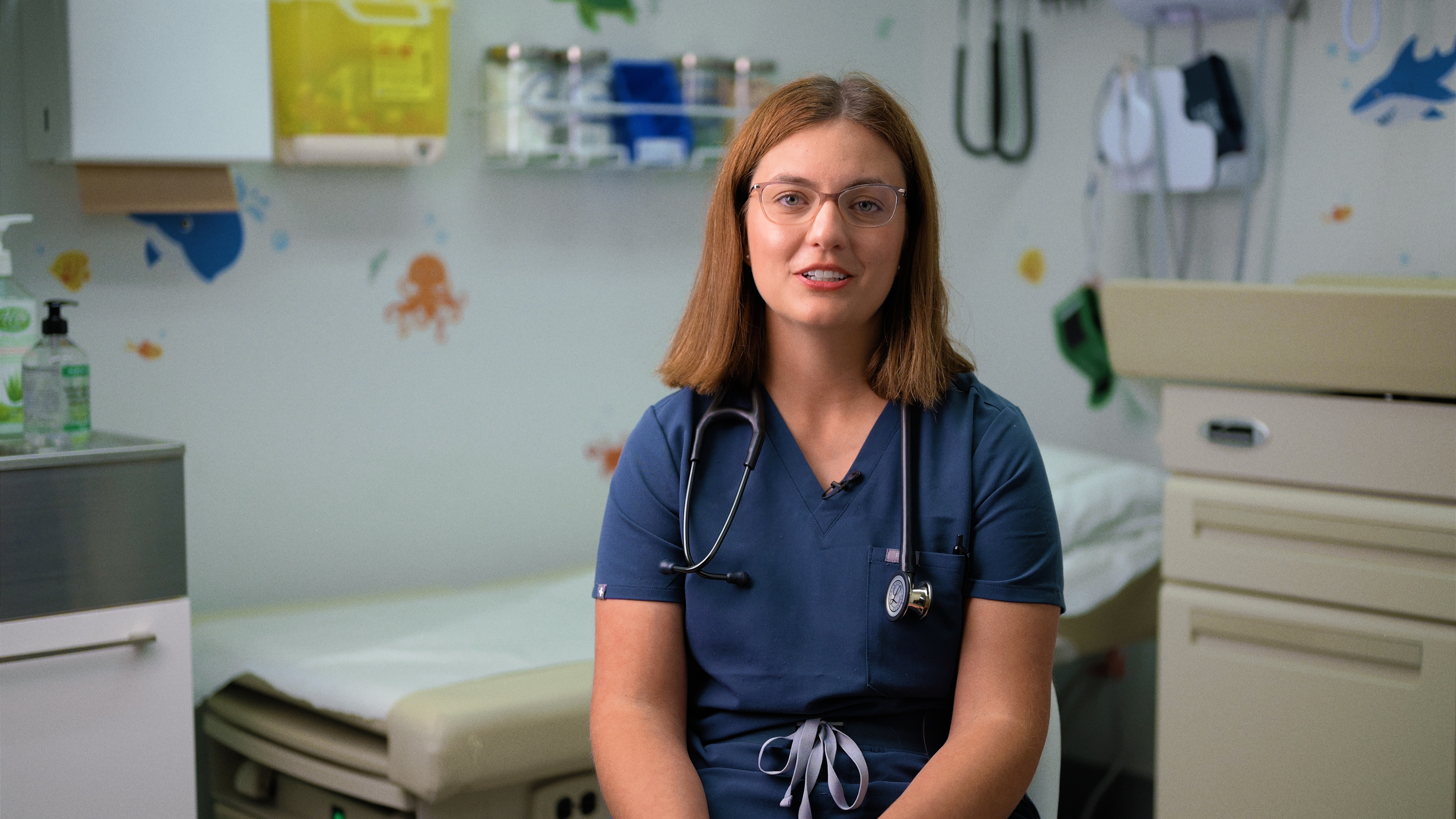 Female physician wearing blue scrubs and stethoscope in a child-friendly examination room