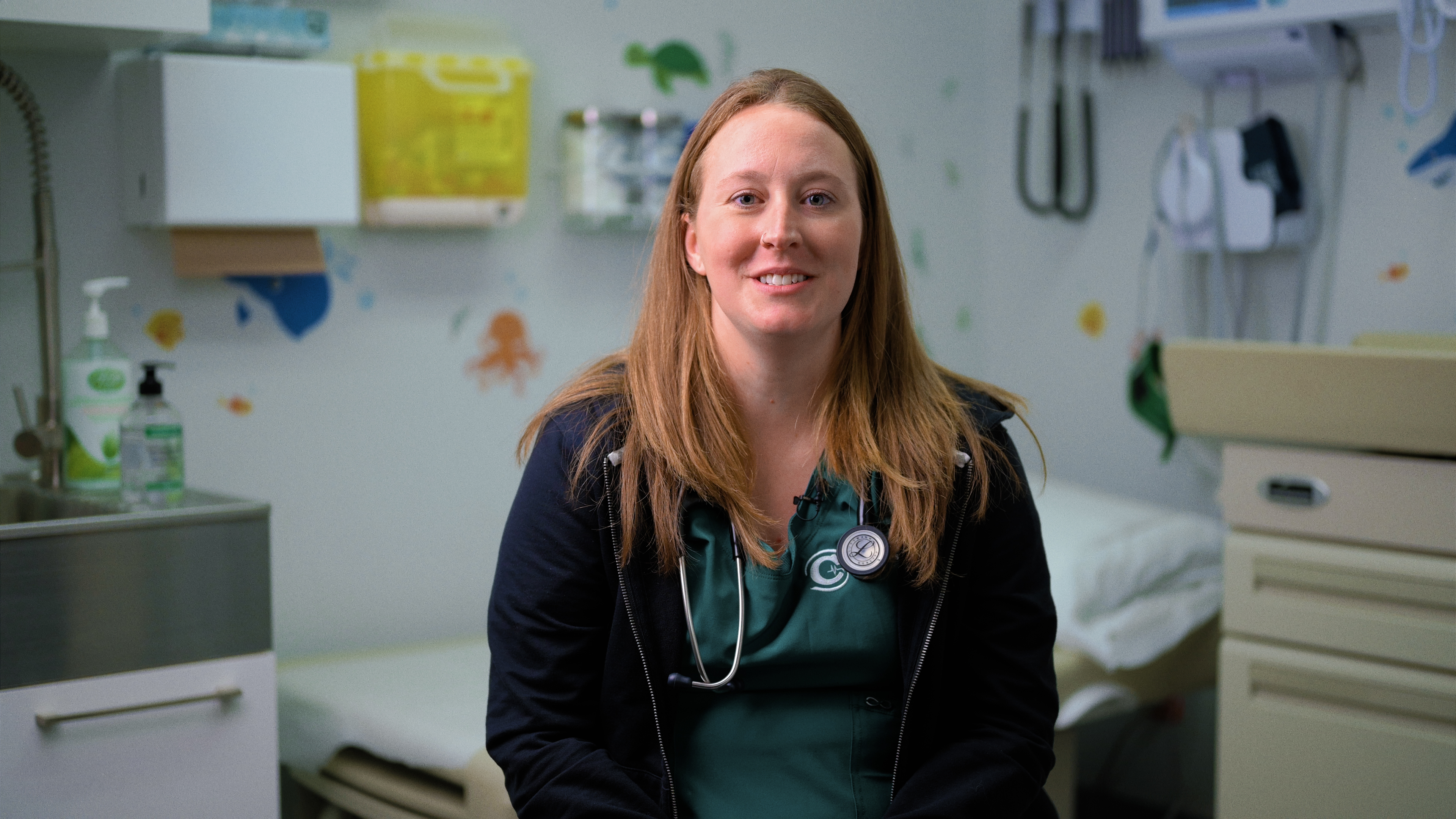 Smiling female physician in scrubs with stethoscope in a pediatric exam room