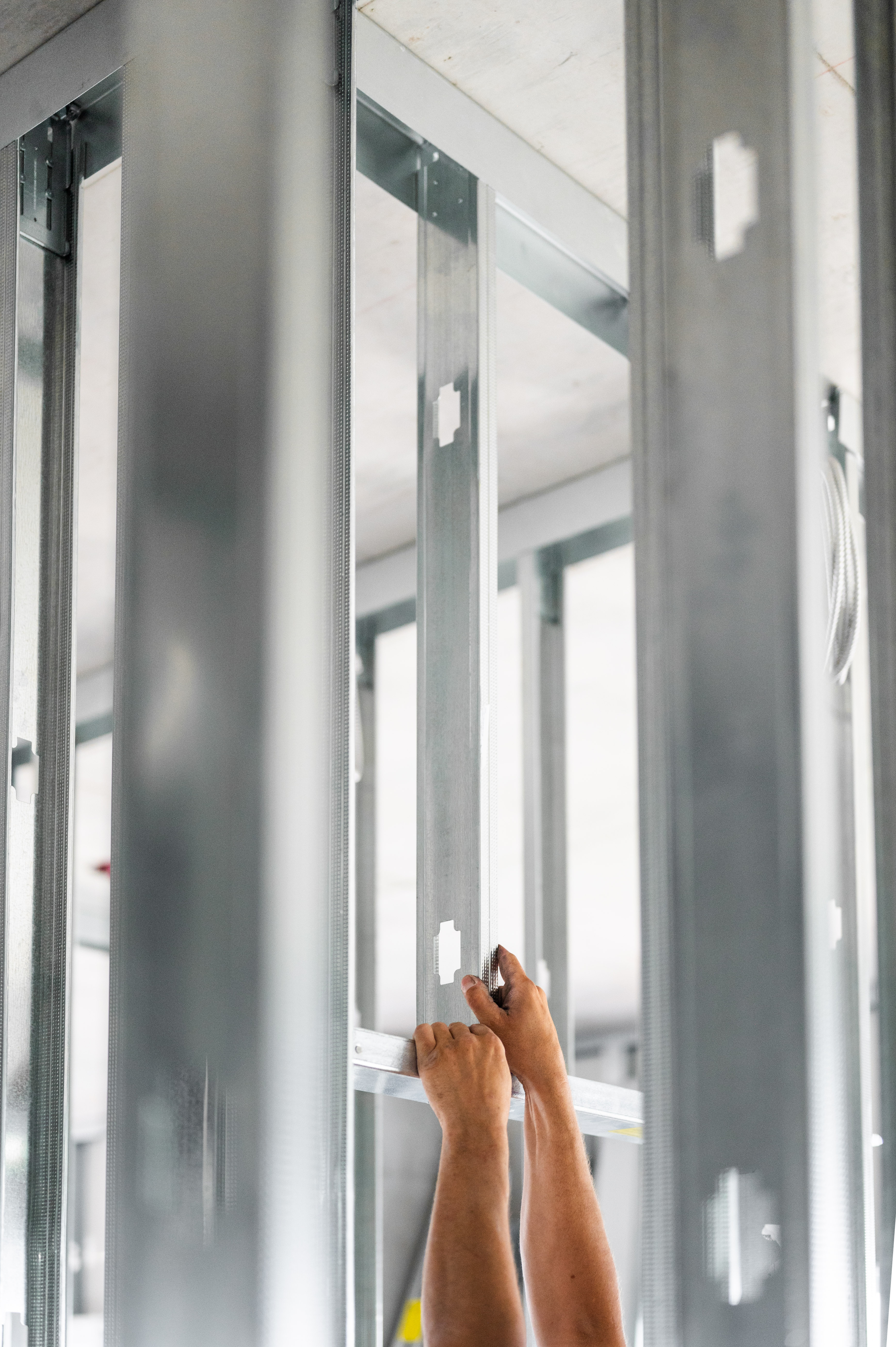 Worker's hands installing metal studs for interior wall framing on a corporate construction site