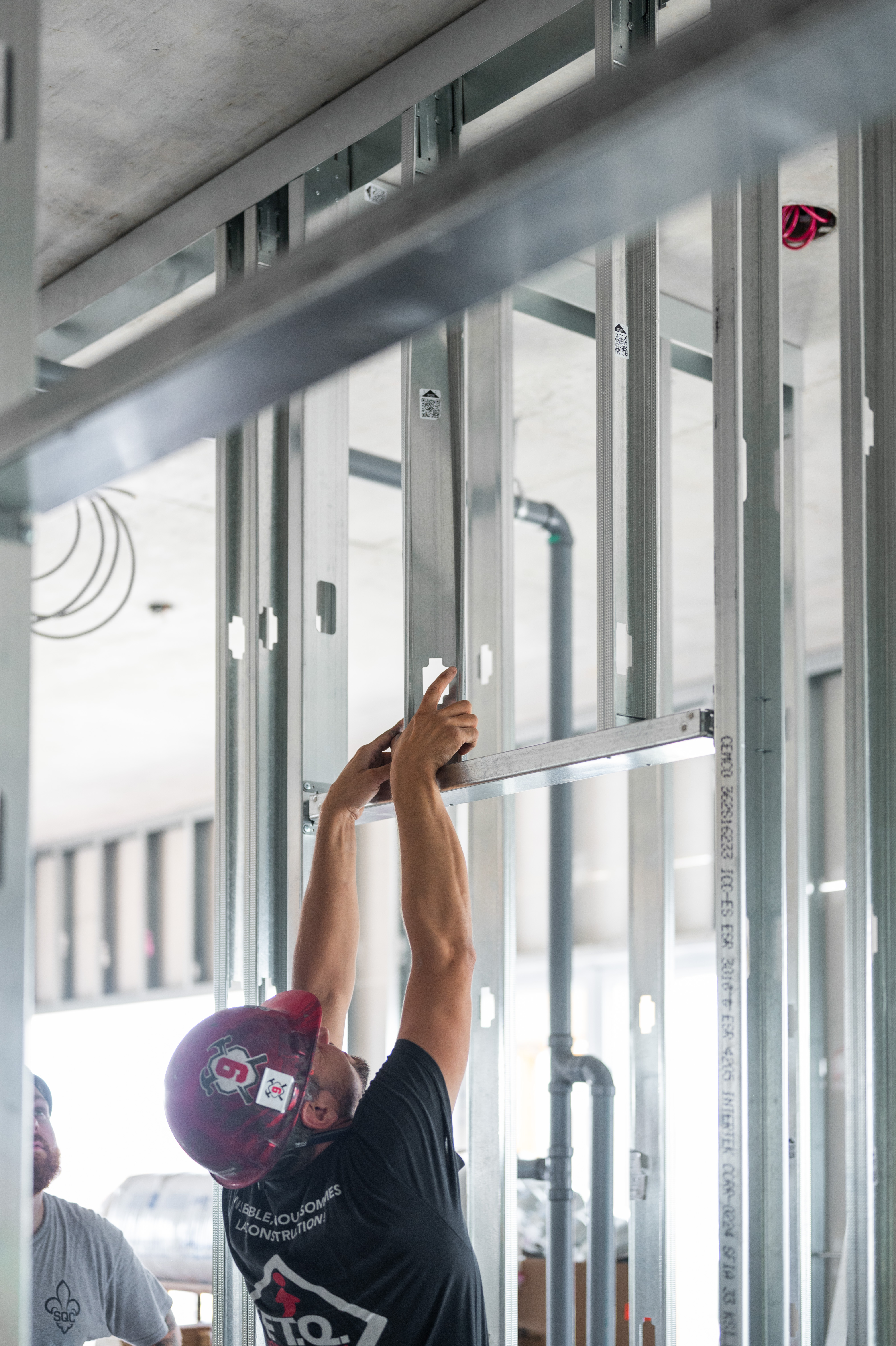 Construction worker wearing a red hard hat installing metal wall studs on site
