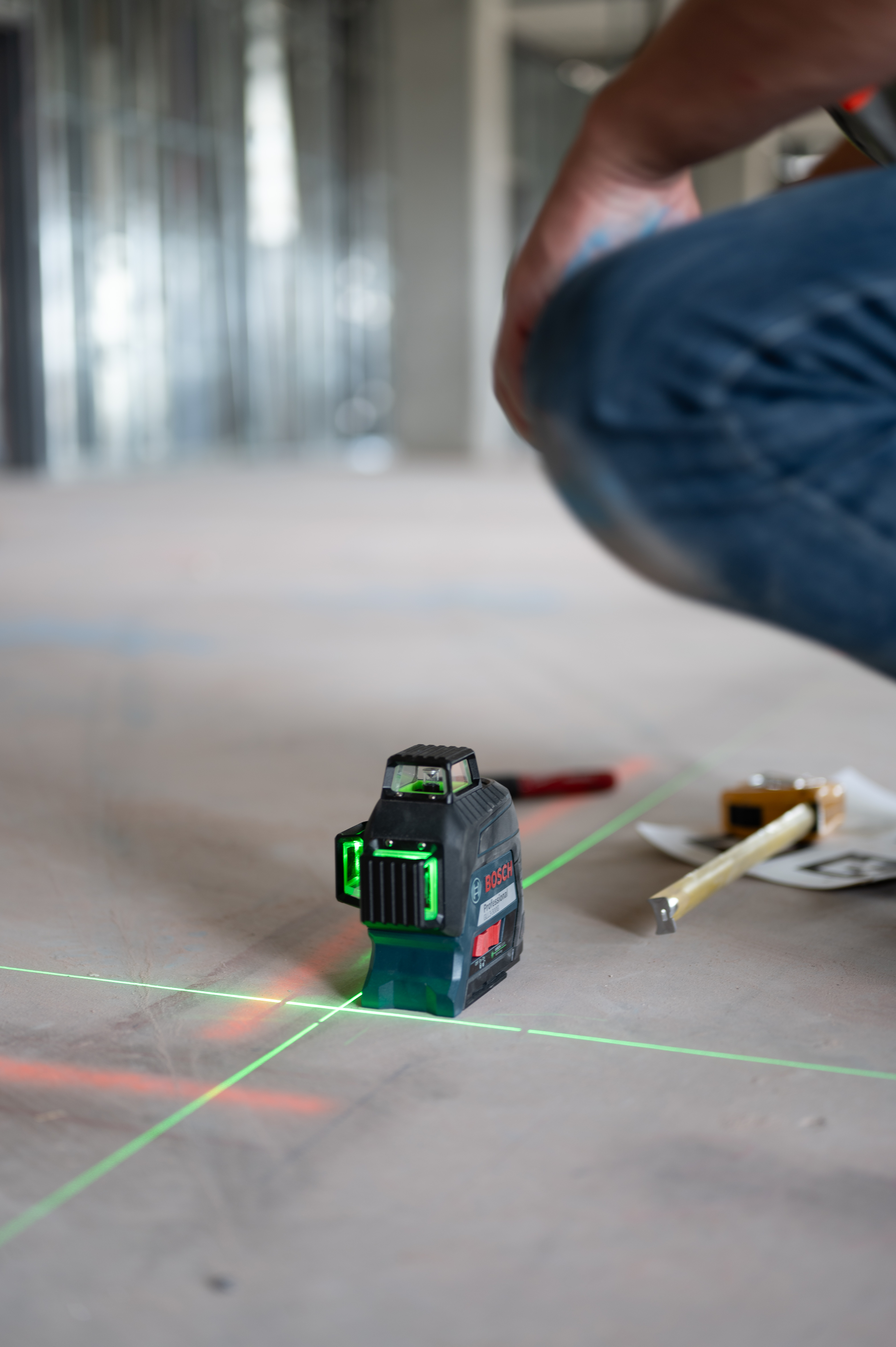 Bosch laser level emitting green laser lines on a concrete floor during construction