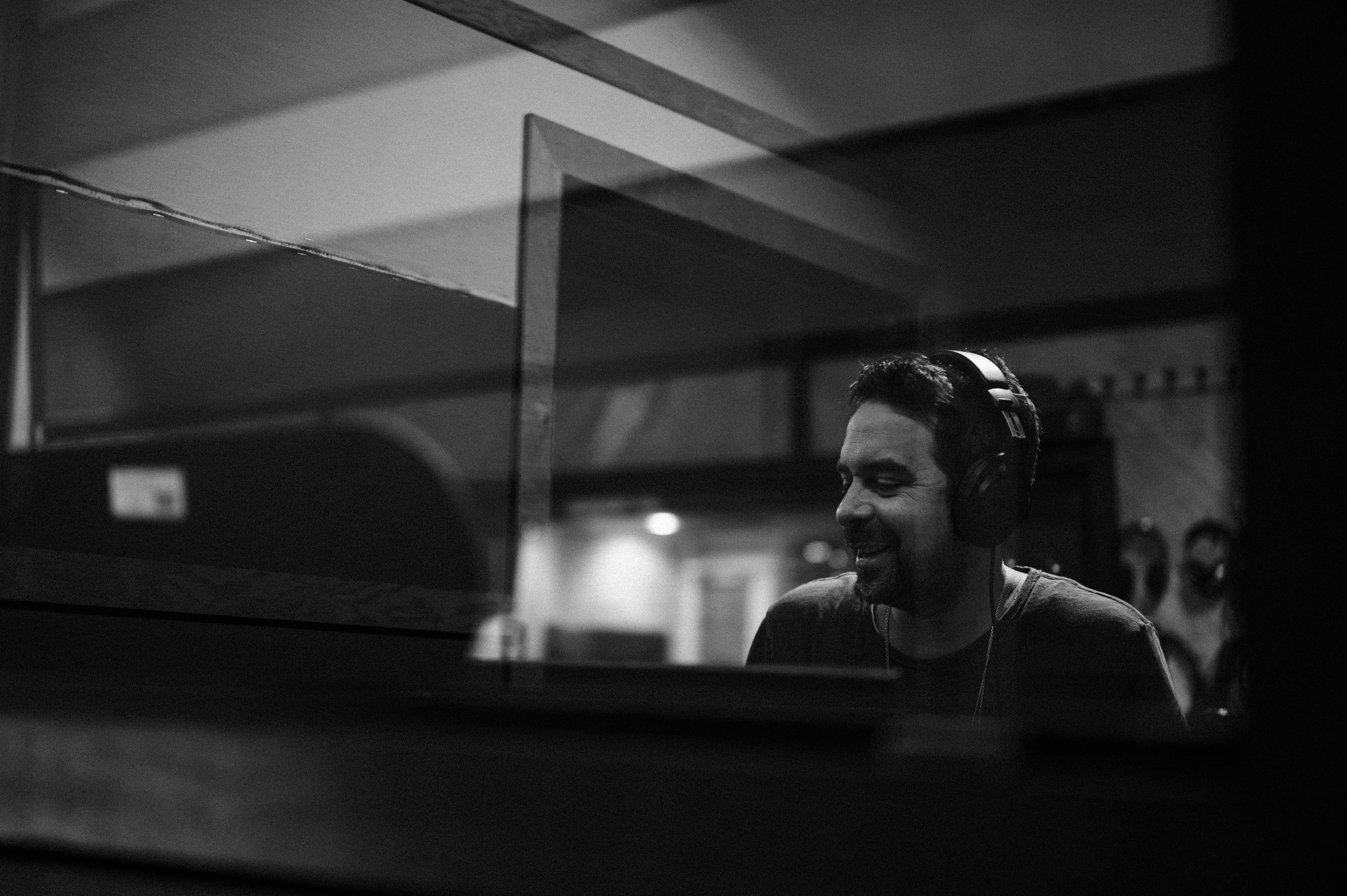 Band member smiling, wearing headphones in a music studio control room