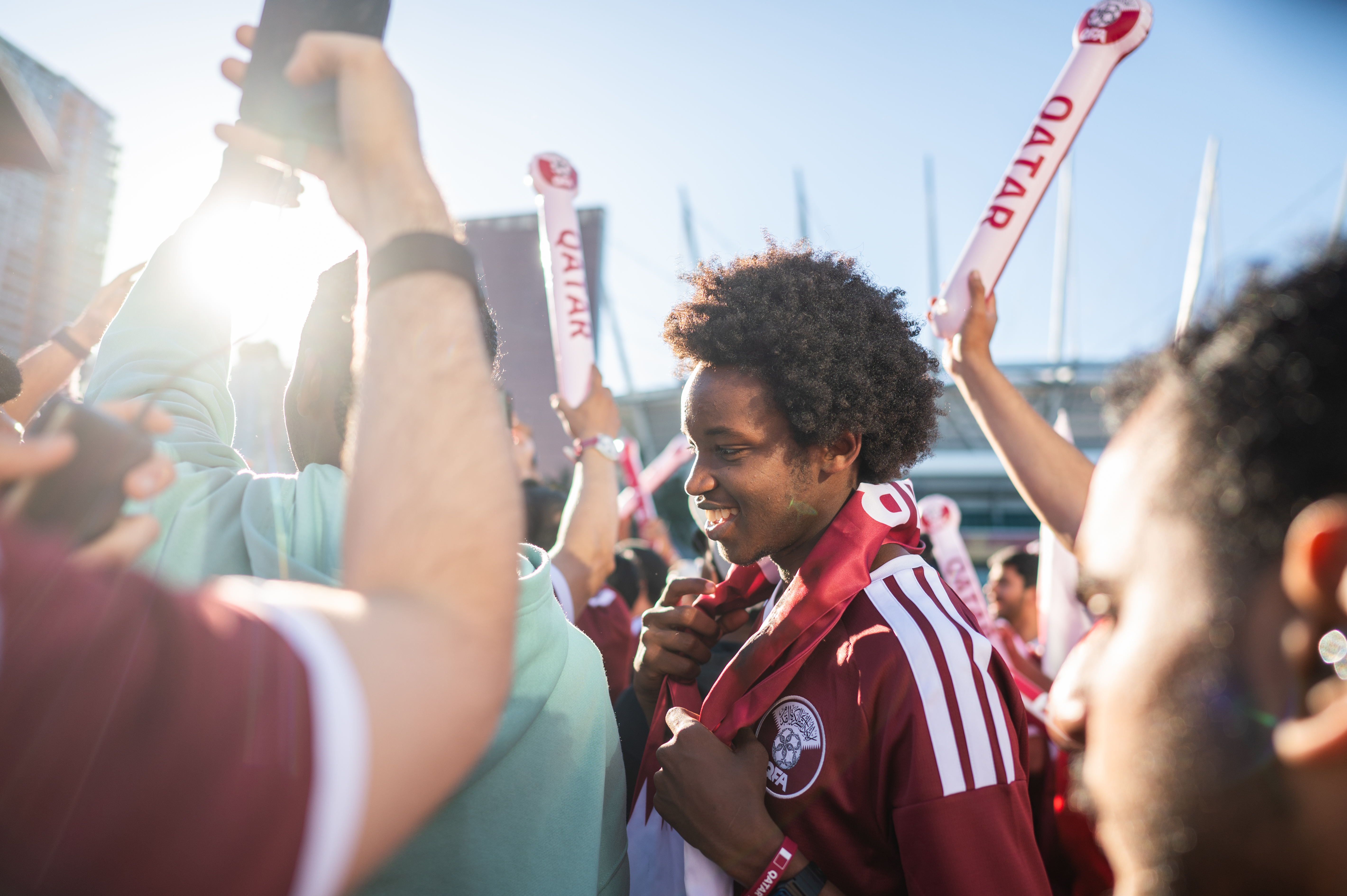 Smiling World Cup fan wearing a maroon jersey and scarf in a bustling crowd