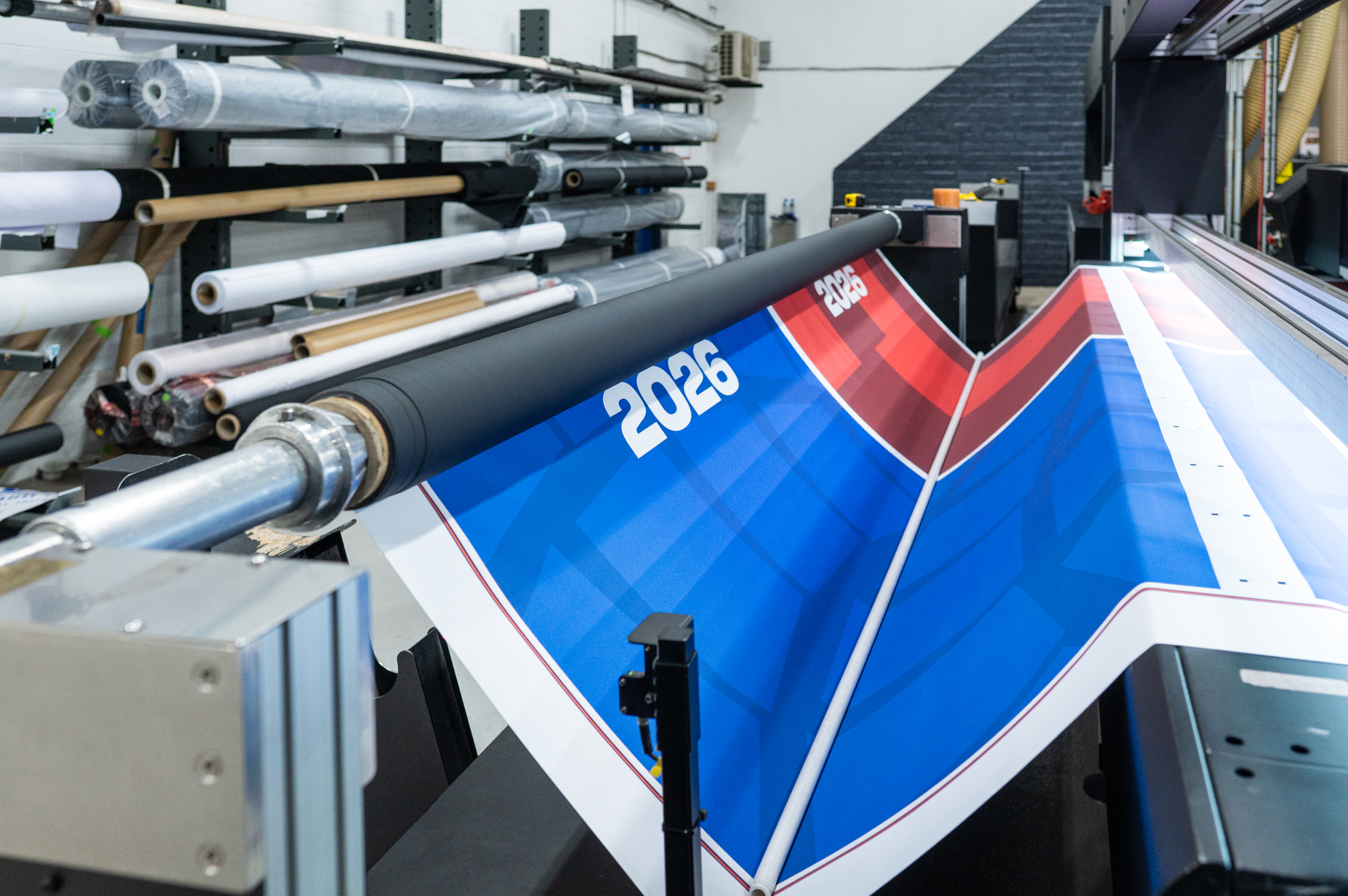 Large format printer dispensing World Cup 2026 graphics onto a banner, with material rolls behind