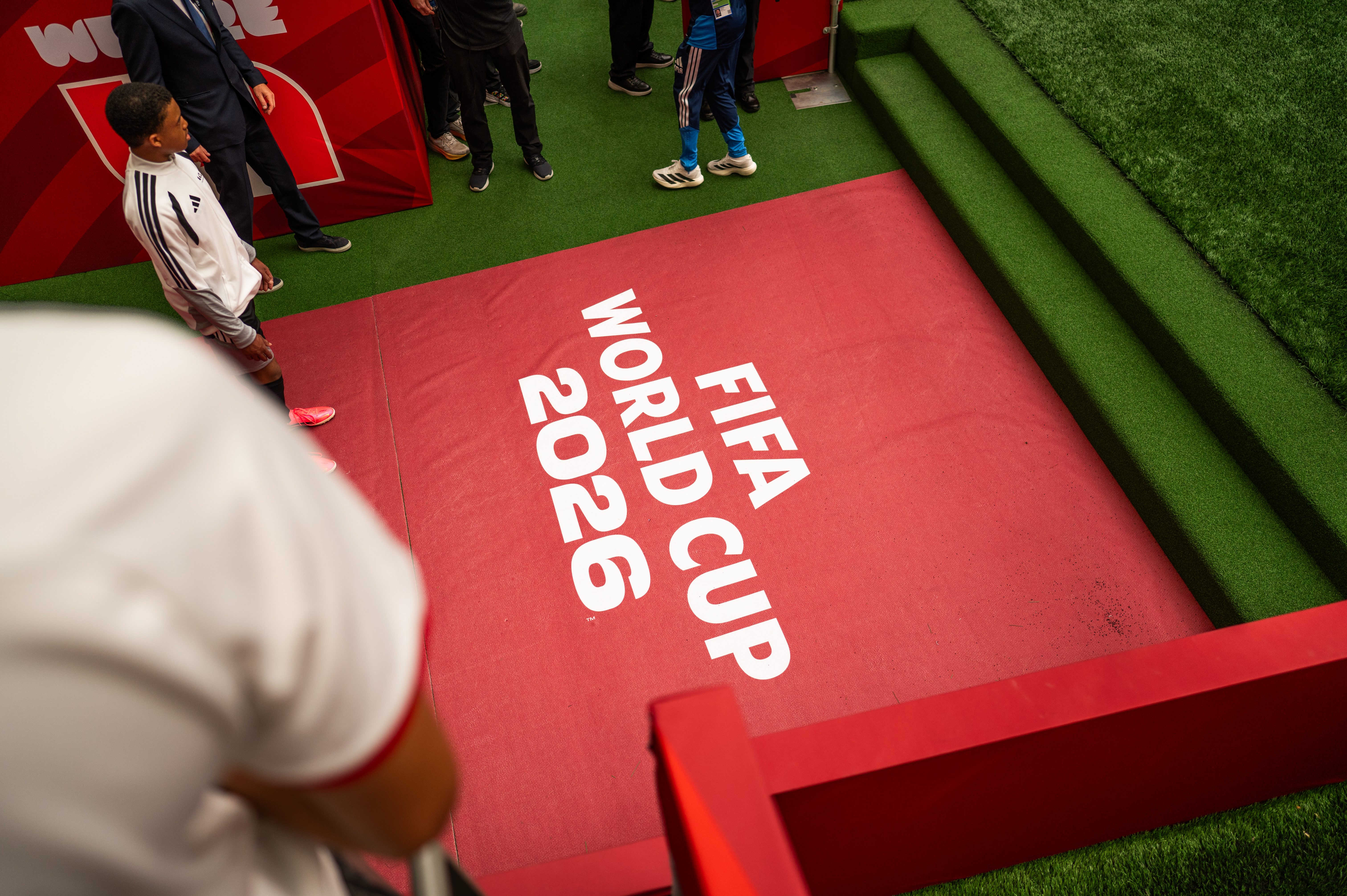 FIFA World Cup 2026 branding on a red floor with artificial turf steps and people
