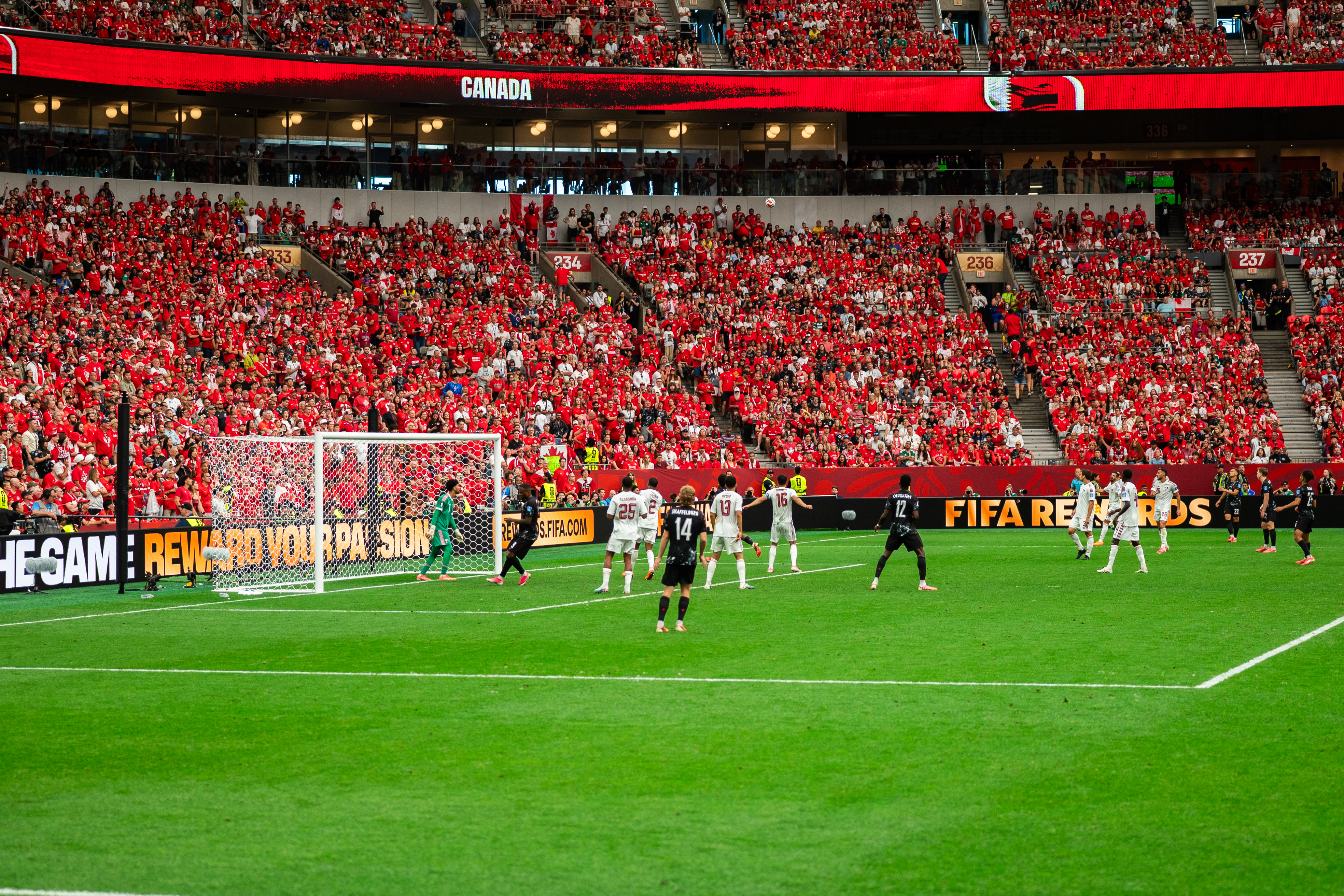 Football match in a large stadium with red-clad crowd and bright green field