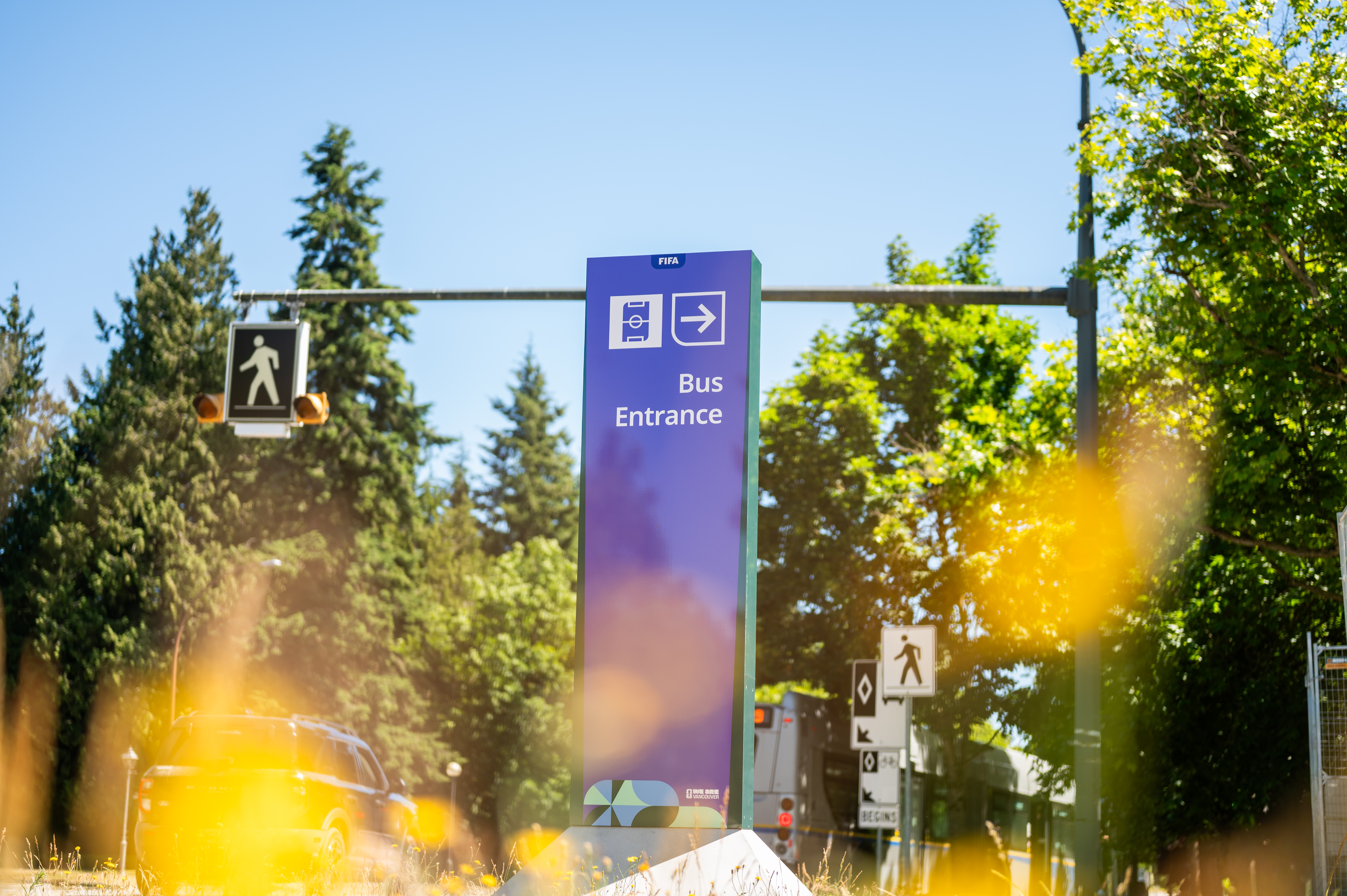 Tall purple FIFA World Cup signage for bus entrance, bright green trees in background