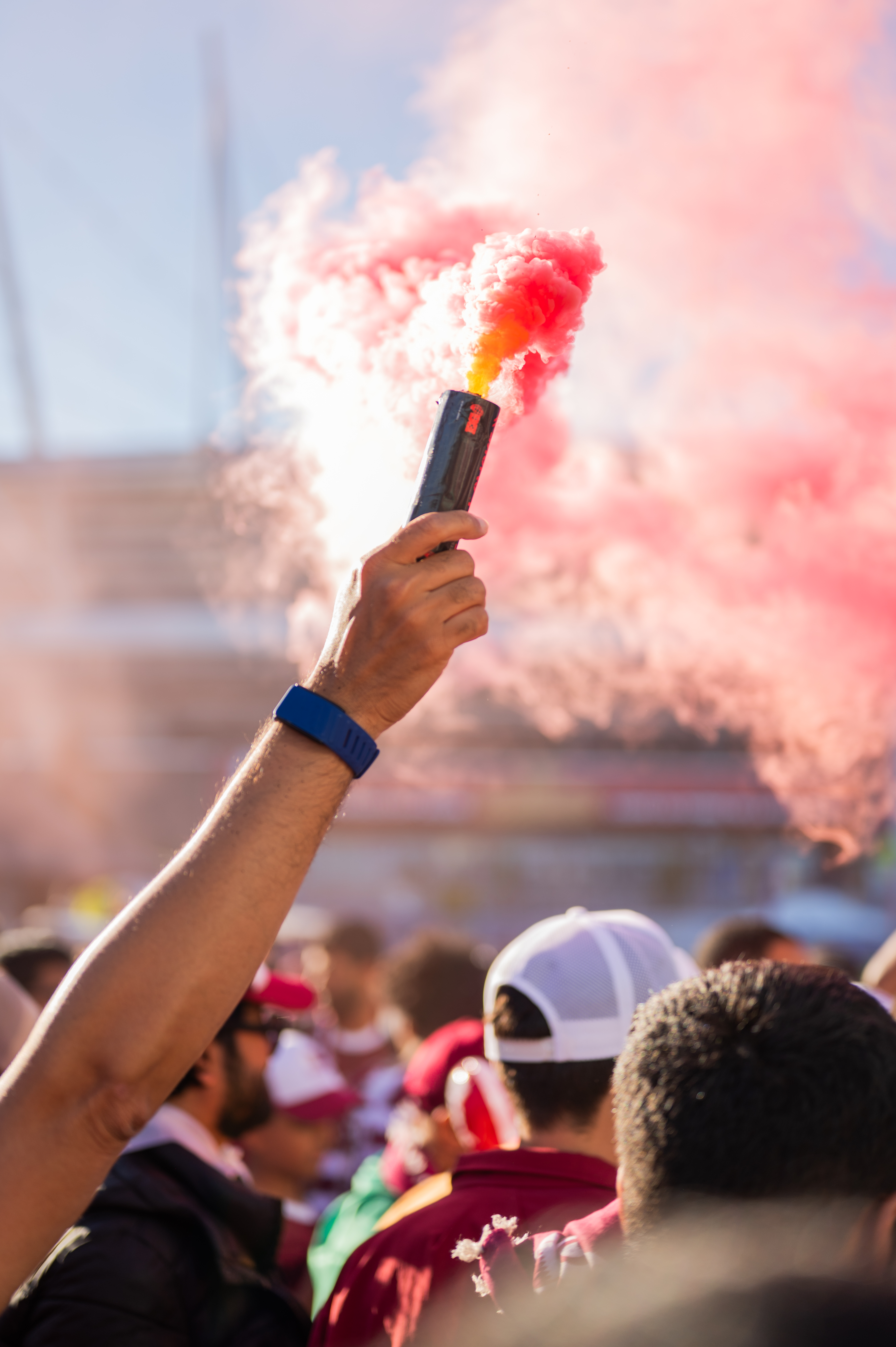 Raised arm holding a smoking red flare at a crowded outdoor event