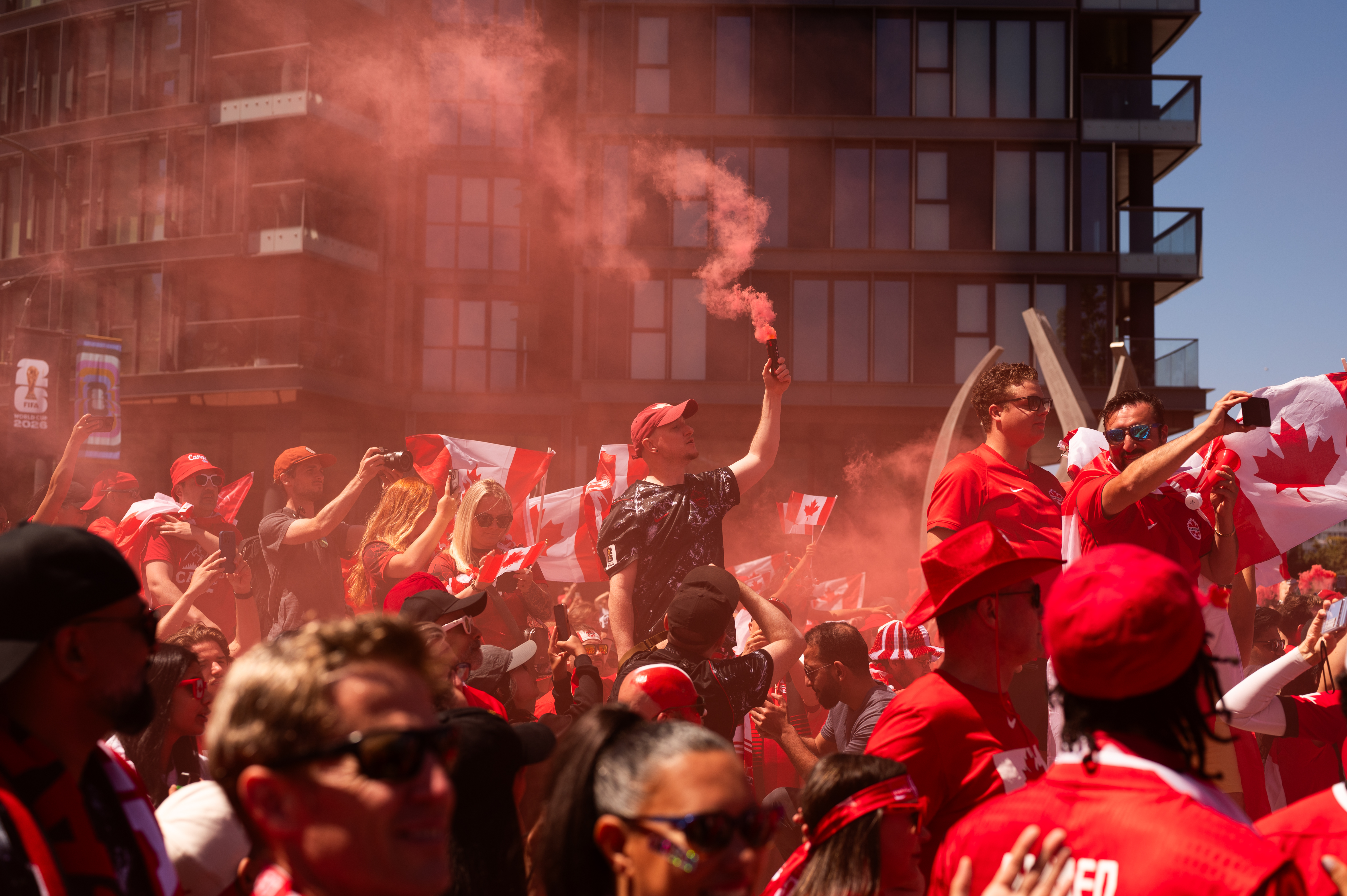 Crowd of Canadian World Cup fans in red shirts and hats, celebrating with red smoke