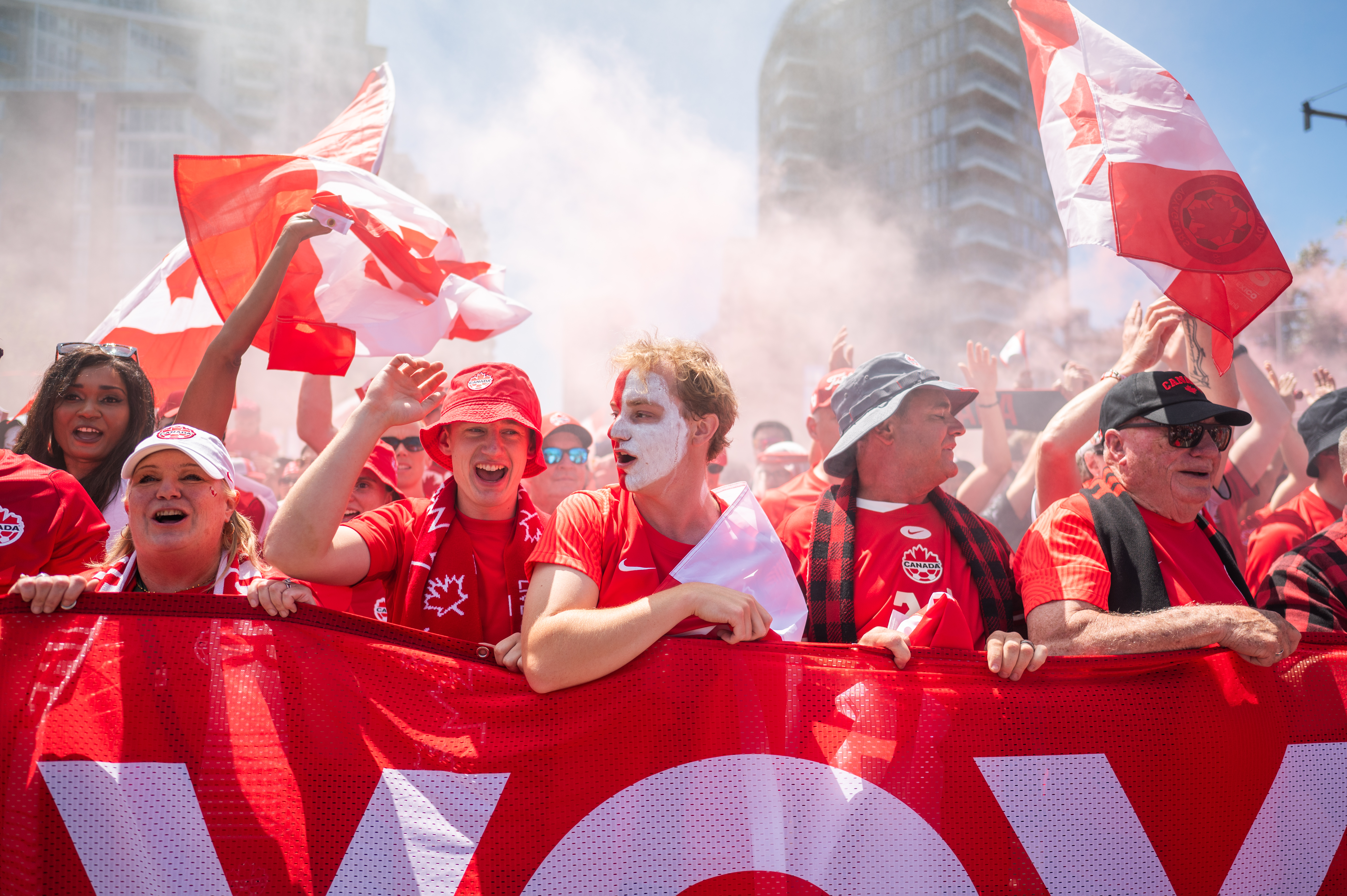 Excited Canadian soccer fans, wearing red, wave flags and cheer during a World Cup event