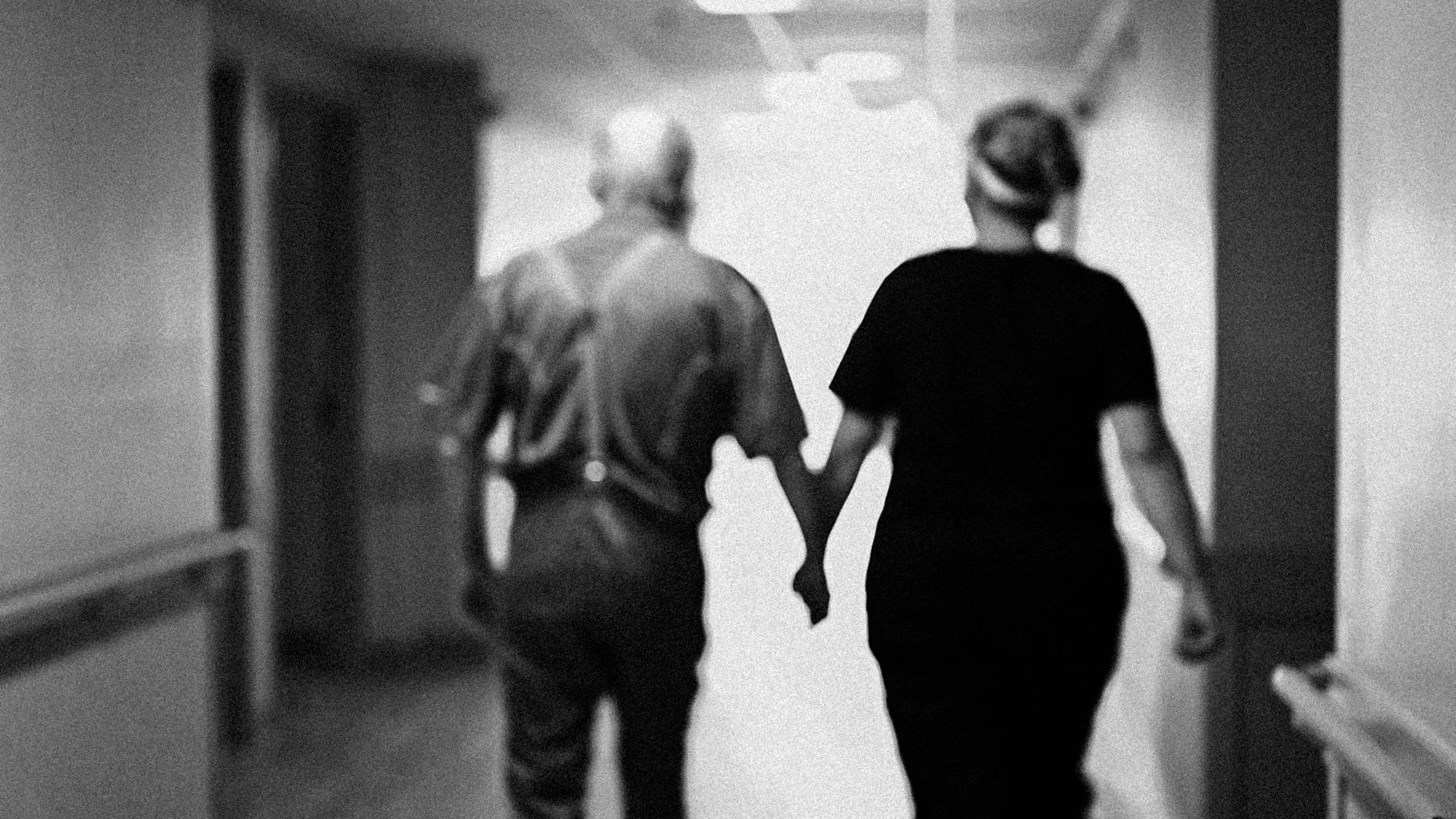 Blurred black and white image of two individuals holding hands, walking down a hallway