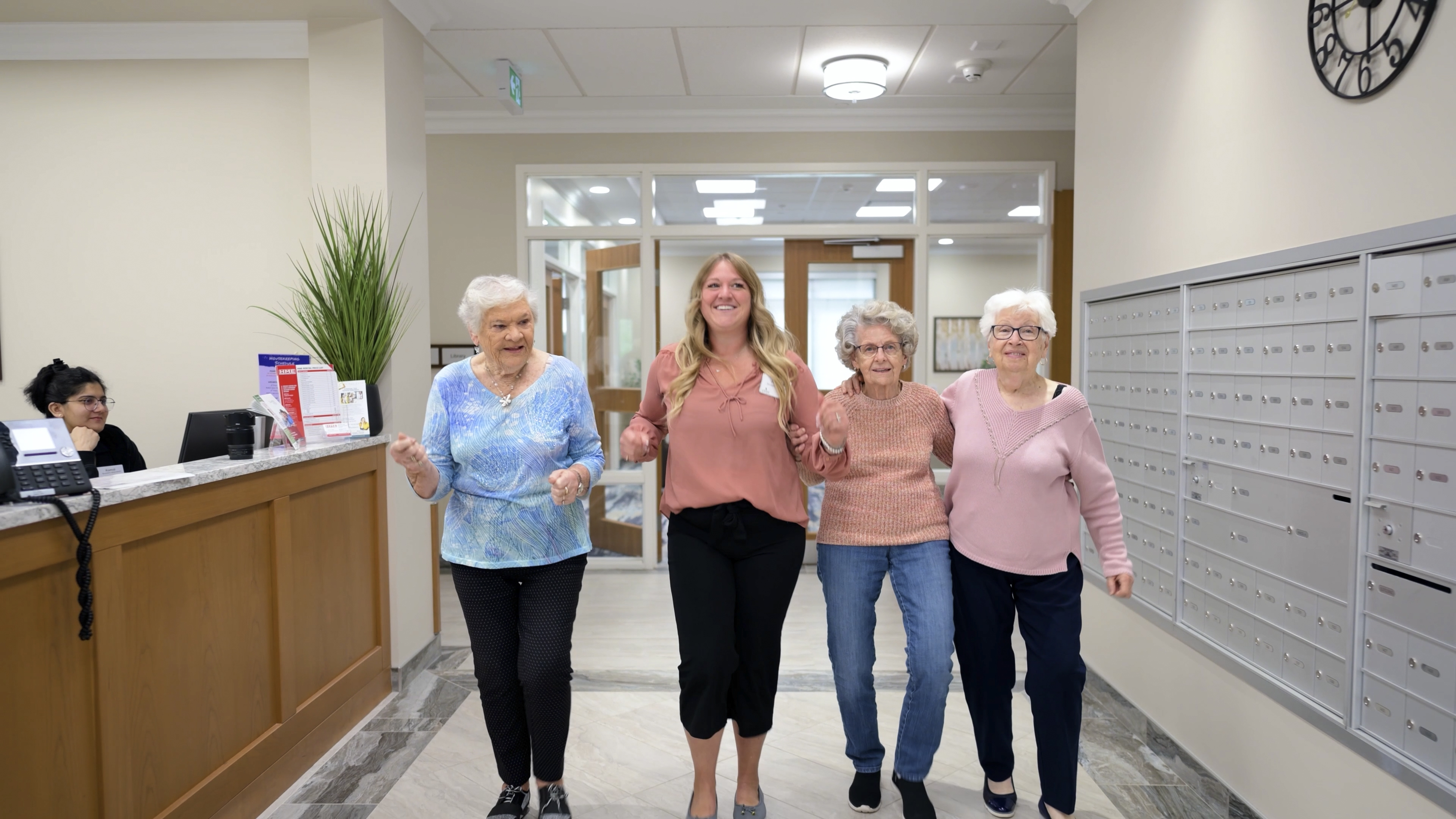 Healthcare team member walks arm-in-arm with three smiling senior residents in a facility hallway