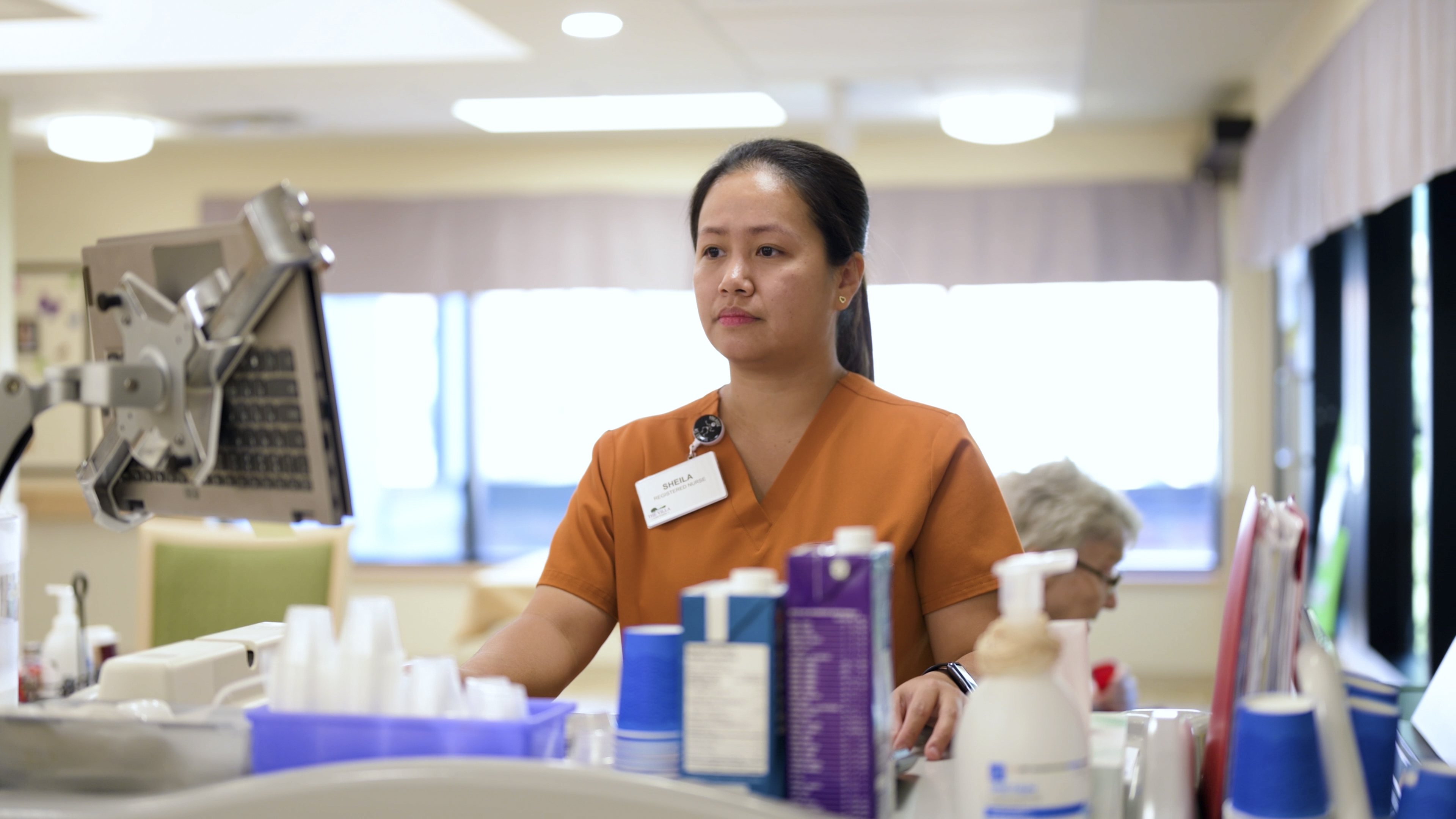 Healthcare professional wearing orange scrubs and a name tag, focused in a bright medical setting